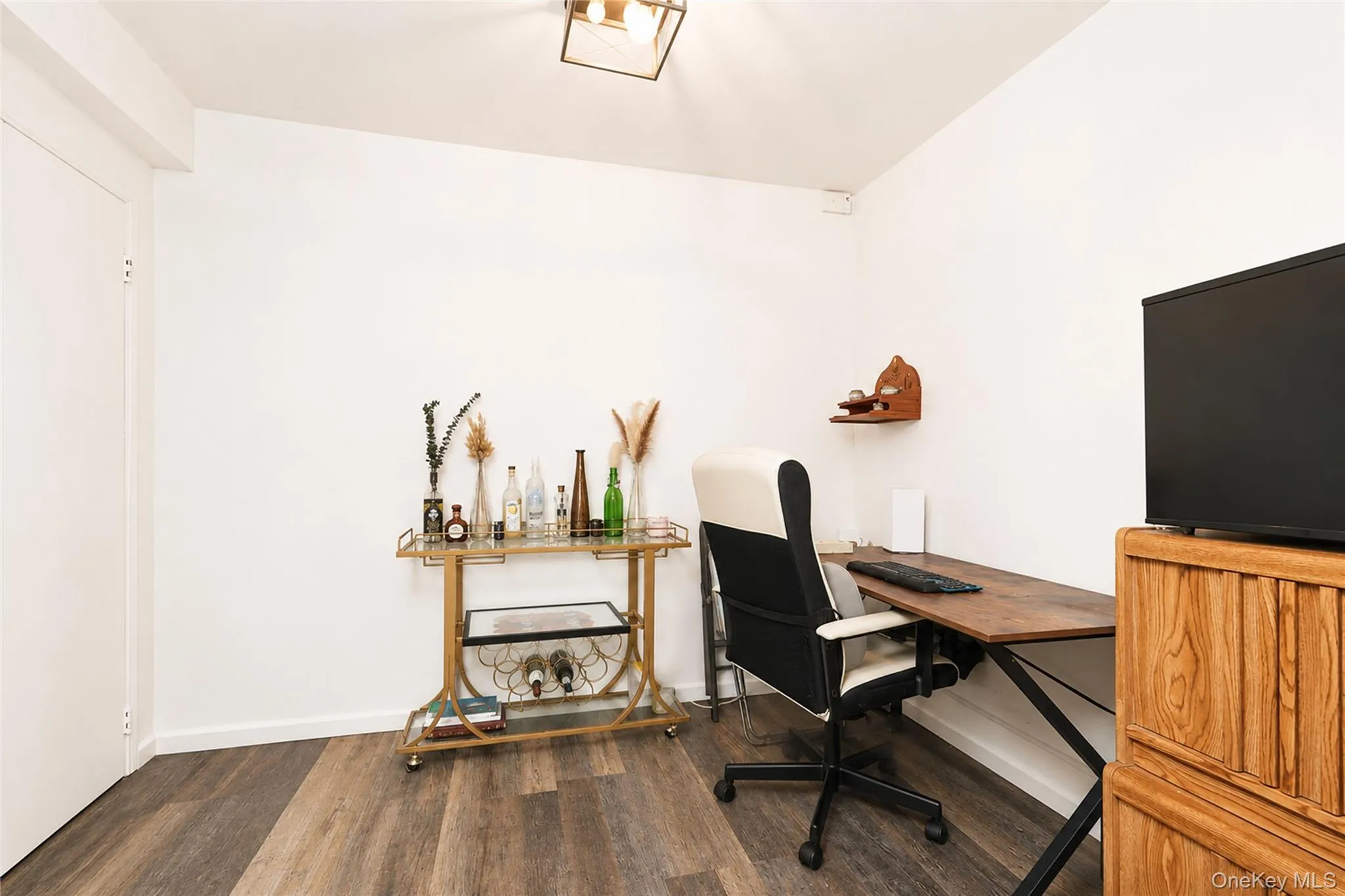Room featuring wood-finish flooring, white walls, and a contemporary ceiling light fixture Room featuring wood-finish flooring, white walls, and a contemporary ceiling light fixture