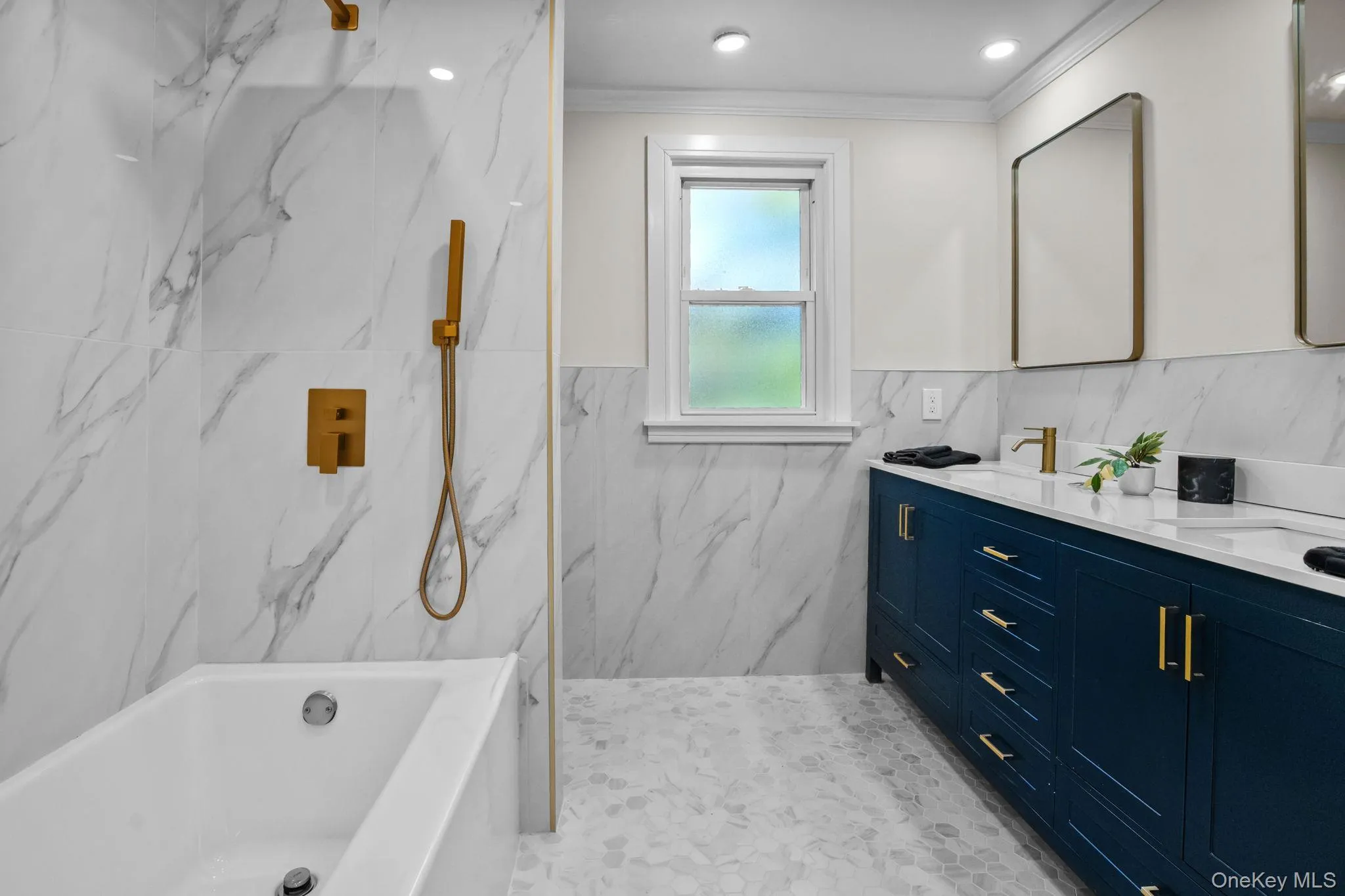 Stunningly renovated full bathroom showcasing floor-to-ceiling marble-inspired tile, a sleek double vanity, and elegant brushed gold fixtures for a touch of modern luxury. Stunningly renovated full bathroom showcasing floor-to-ceiling marble-inspired tile, a sleek double vanity, and elegant brushed gold fixtures for a touch of modern luxury.