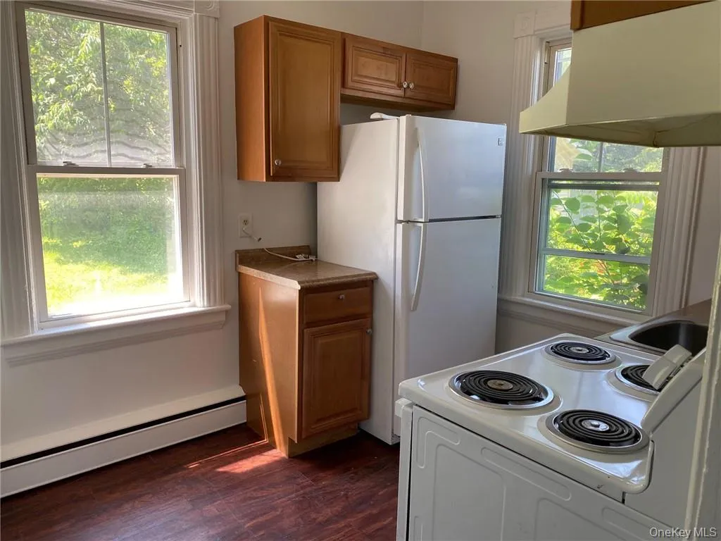 Kitchen with a baseboard heating unit, stove, white refrigerator, range hood, and dark wood-style floors Kitchen with a baseboard heating unit, stove, white refrigerator, range hood, and dark wood-style floors