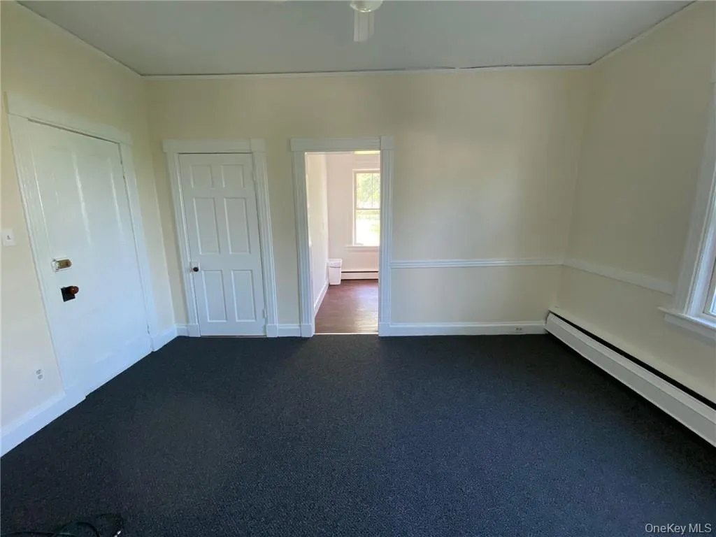 Unfurnished living room featuring baseboard heating and dark carpet Unfurnished living room featuring baseboard heating and dark carpet