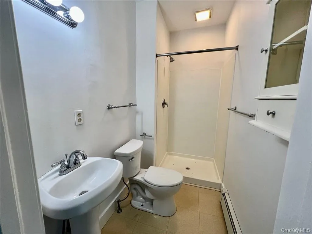 Bathroom featuring tile flooring, a baseboard radiator, a shower, sink, and toilet Bathroom featuring tile flooring, a baseboard radiator, a shower, sink, and toilet