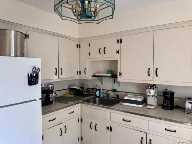 Kitchen featuring white cabinetry with dark hardware, a stainless steel sink, and a stained glass-style ceiling light fixture Kitchen featuring white cabinetry with dark hardware, a stainless steel sink, and a stained glass-style ceiling light fixture
