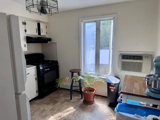White cabinetry with black hardware, black gas range with coordinating range hood, vinyl tile flooring, window-mounted air conditioning unit, and a prominent window and eat in area White cabinetry with black hardware, black gas range with coordinating range hood, vinyl tile flooring, window-mounted air conditioning unit, and a prominent window and eat in area