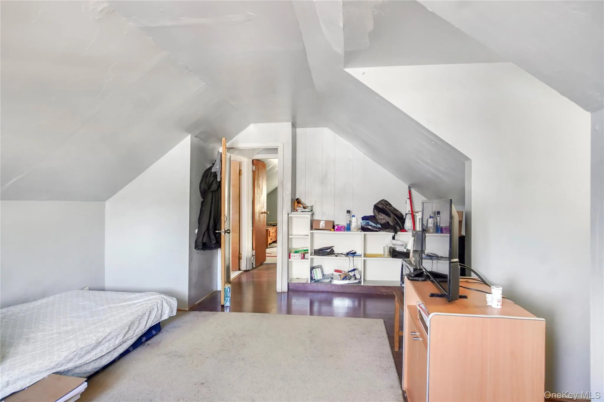 Spacious room featuring sloped ceilings, light-toned wall finishes, wood-finish flooring, and a doorway leading to an additional area Spacious room featuring sloped ceilings, light-toned wall finishes, wood-finish flooring, and a doorway leading to an additional area