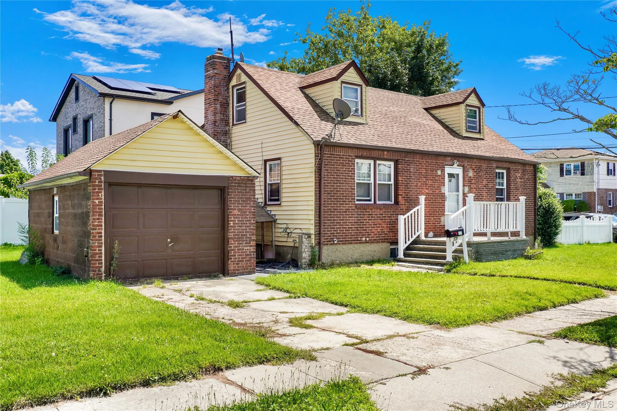 Brick and siding exterior featuring a covered front porch with white railings, a detached single-car garage, and a pitched roofline with dormer windows Brick and siding exterior featuring a covered front porch with white railings, a detached single-car garage, and a pitched roofline with dormer windows