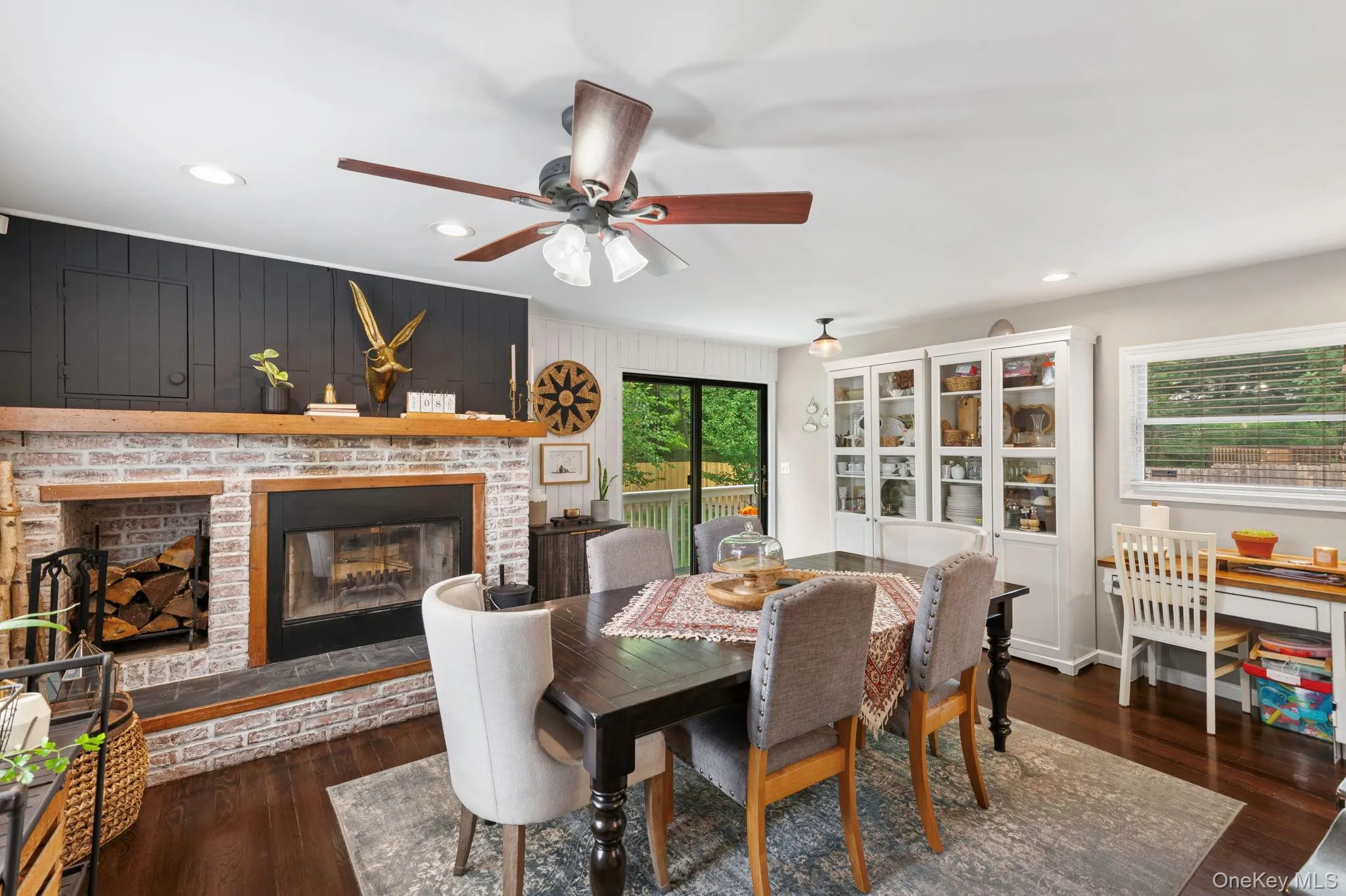 Brick fireplace with a dark wood mantle, wood-finish flooring, recessed lighting, and a ceiling fan Brick fireplace with a dark wood mantle, wood-finish flooring, recessed lighting, and a ceiling fan