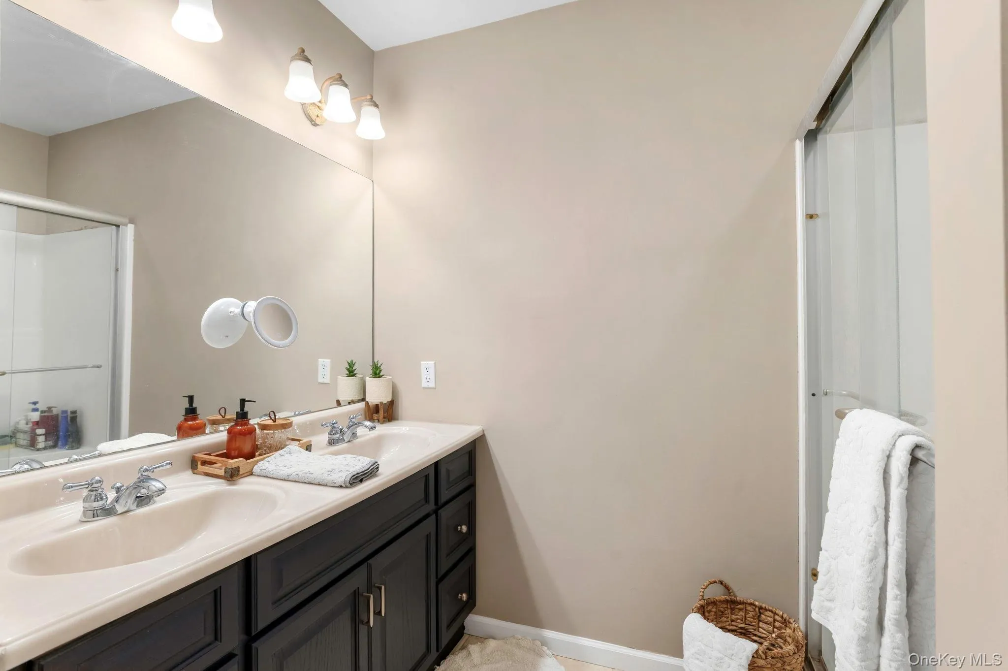 Double vanity with integrated sinks, extensive wall mirror, three-light fixture, and glass-enclosed shower Double vanity with integrated sinks, extensive wall mirror, three-light fixture, and glass-enclosed shower