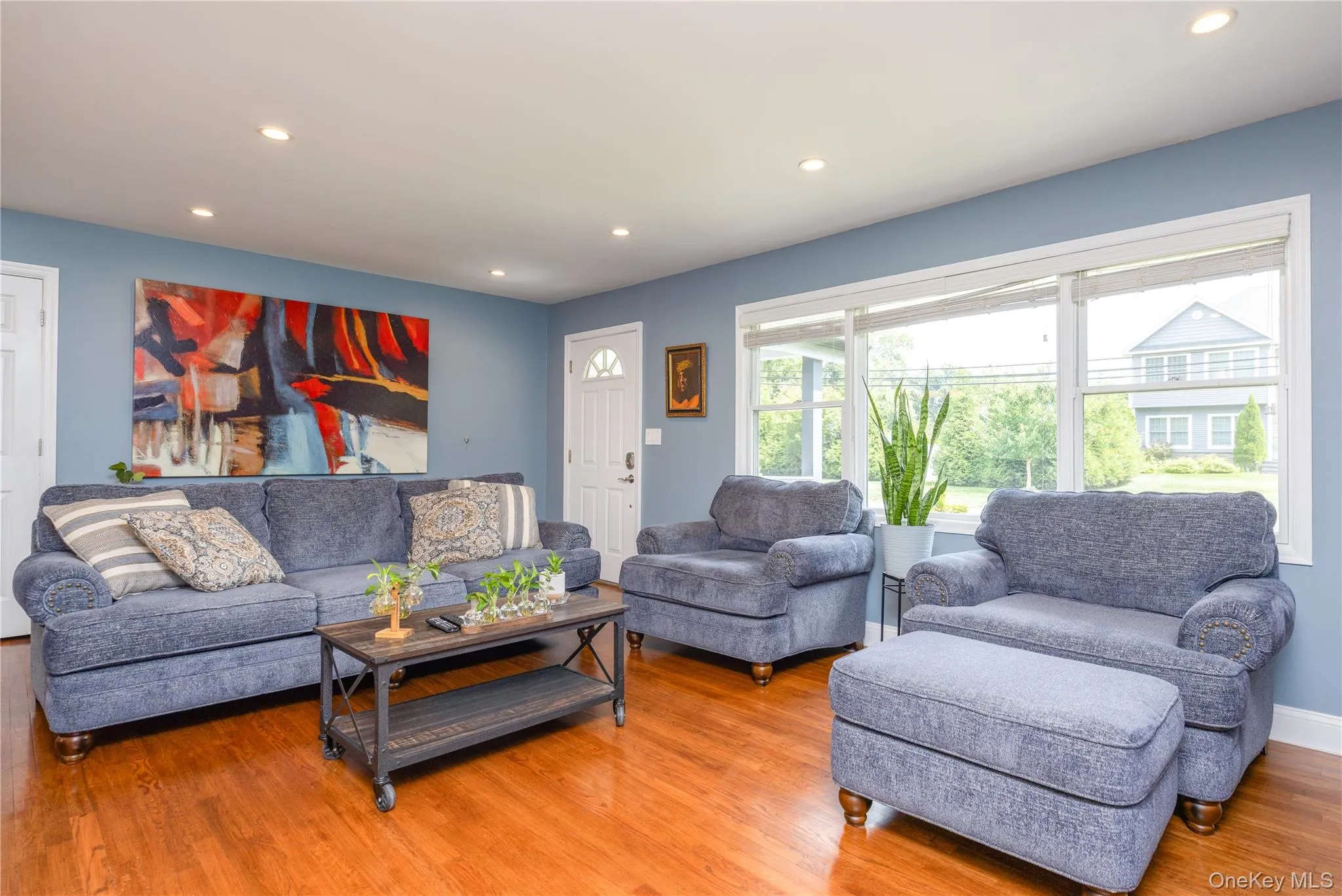 Recessed lighting illuminates the open living area featuring wood-finish flooring, a white paneled door, and a multi-pane window Recessed lighting illuminates the open living area featuring wood-finish flooring, a white paneled door, and a multi-pane window