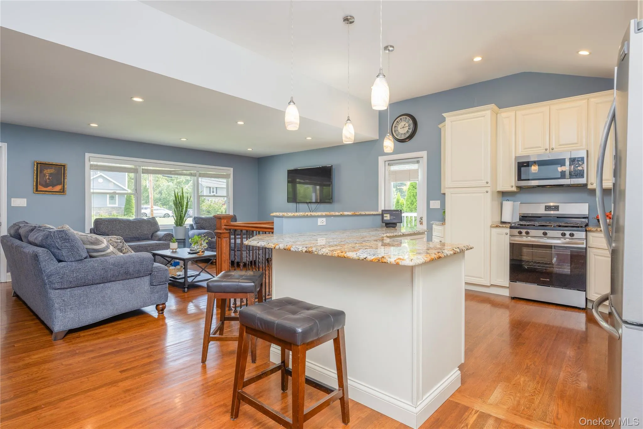 Open-concept living space featuring wood-finish flooring, recessed lighting, a kitchen island with stone countertop, and stainless steel appliances Open-concept living space featuring wood-finish flooring, recessed lighting, a kitchen island with stone countertop, and stainless steel appliances