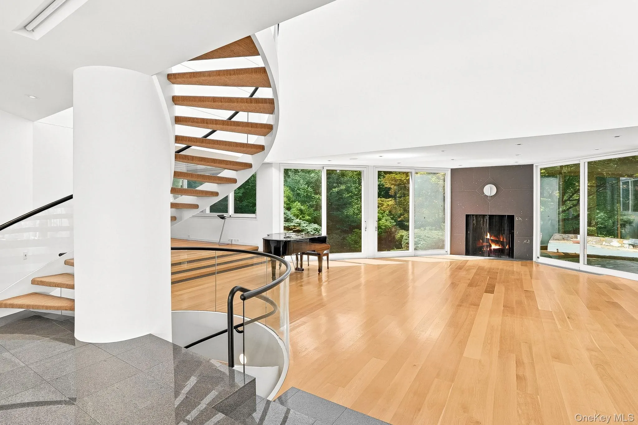 Striking architectural design defines the main living area, featuring an elegant curved staircase, a cozy fireplace, and space for a grand piano. Striking architectural design defines the main living area, featuring an elegant curved staircase, a cozy fireplace, and space for a grand piano.