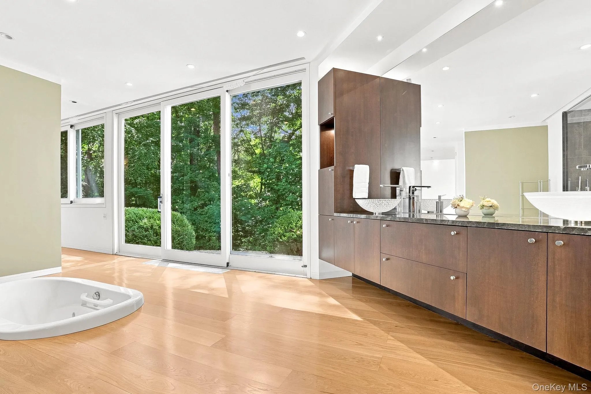 A spa-like master bathroom featuring a wood vanity, an inset jetted tub, and sliding glass doors with serene nature views. A spa-like master bathroom featuring a wood vanity, an inset jetted tub, and sliding glass doors with serene nature views.