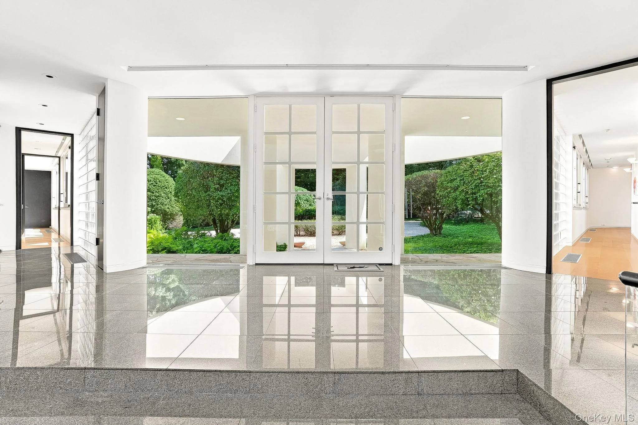 Polished granite-style tile floors and expansive floor-to-ceiling windows flood this striking modern foyer with lush green views. Polished granite-style tile floors and expansive floor-to-ceiling windows flood this striking modern foyer with lush green views.