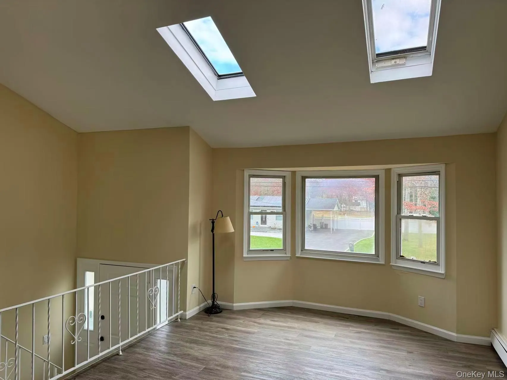 Unfurnished room featuring light wood-type flooring, a baseboard heating unit, a skylight, and lofted ceiling Unfurnished room featuring light wood-type flooring, a baseboard heating unit, a skylight, and lofted ceiling