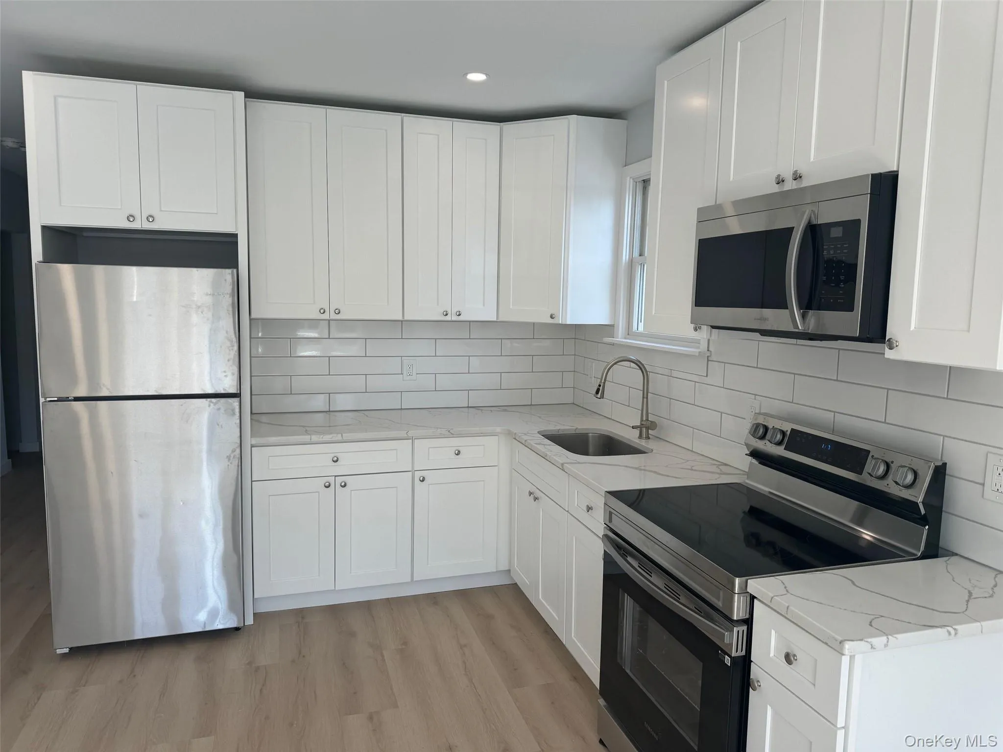Kitchen with stainless steel appliances, a sink, white cabinetry, light wood-type flooring, and light stone counters Kitchen with stainless steel appliances, a sink, white cabinetry, light wood-type flooring, and light stone counters