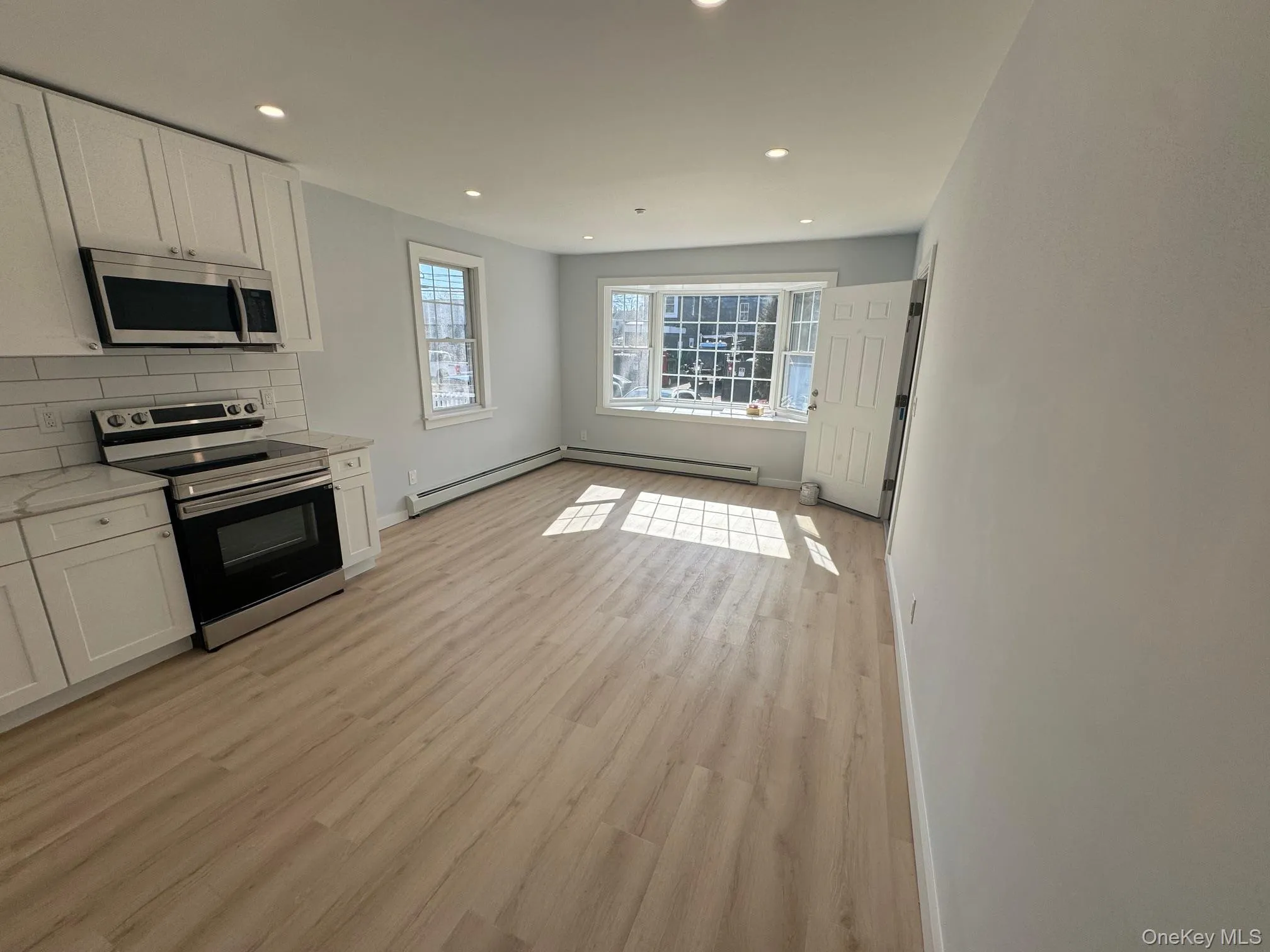 Kitchen with stainless steel appliances, white cabinets, recessed lighting, a baseboard heating unit, and decorative backsplash Kitchen with stainless steel appliances, white cabinets, recessed lighting, a baseboard heating unit, and decorative backsplash