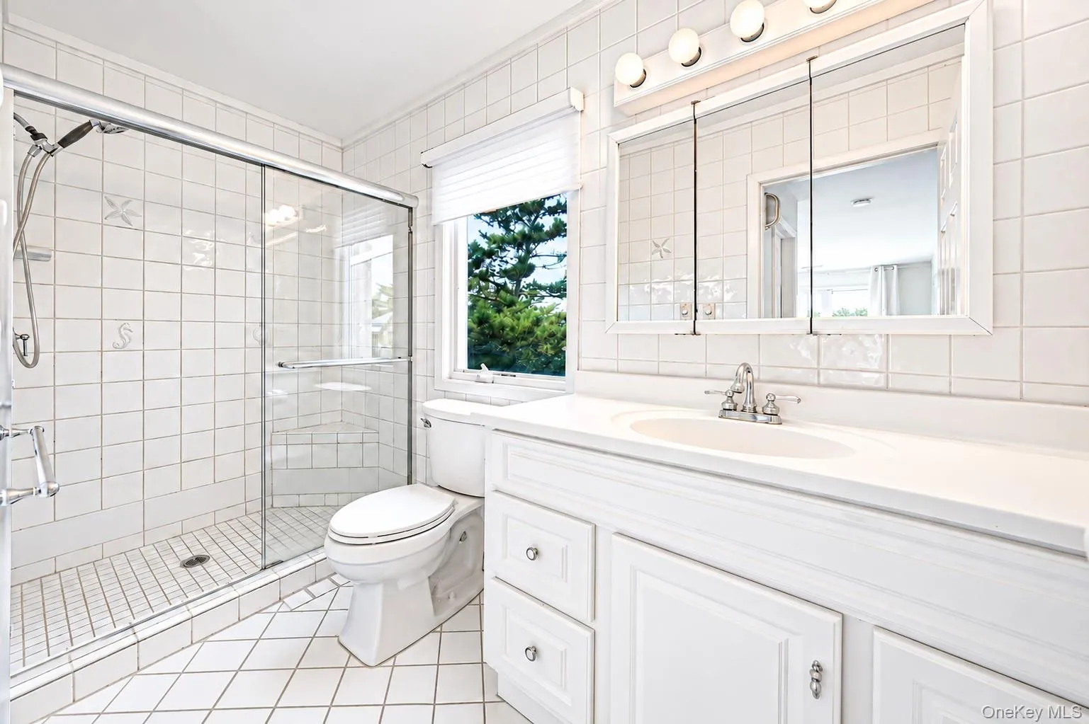 White tiled bathroom featuring a glass-enclosed shower, single vanity