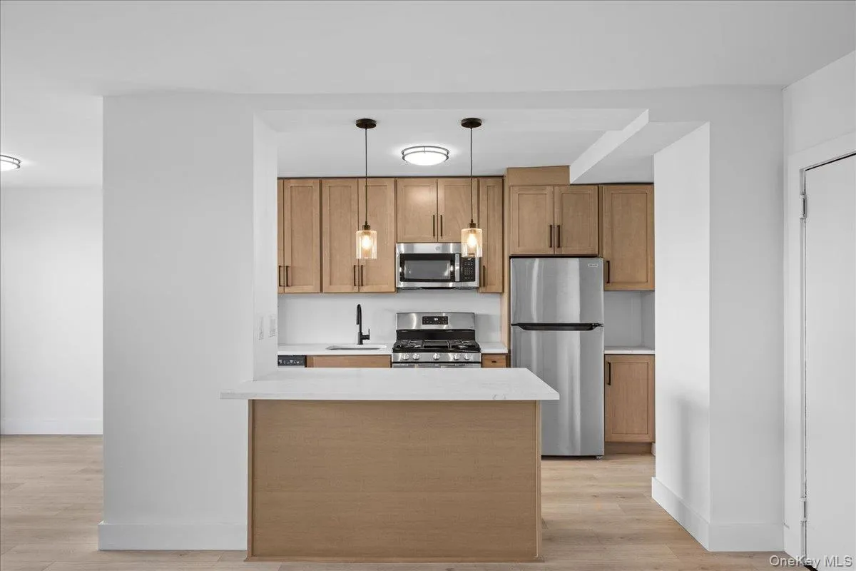 Modern kitchen featuring light wood-finish cabinetry, stainless steel appliances, white countertops, and vinyl flooring Modern kitchen featuring light wood-finish cabinetry, stainless steel appliances, white countertops, and vinyl flooring