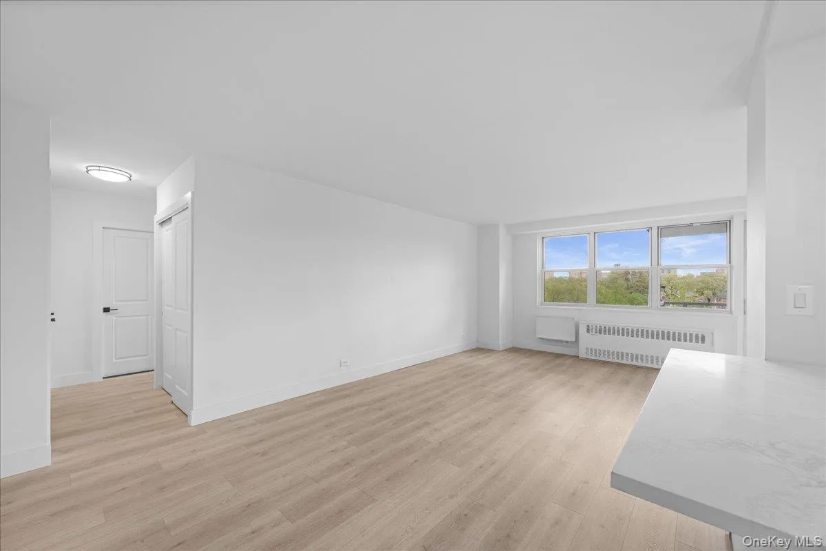 Open concept living space with light-tone vinyl flooring, white walls, and a large window Open concept living space with light-tone vinyl flooring, white walls, and a large window
