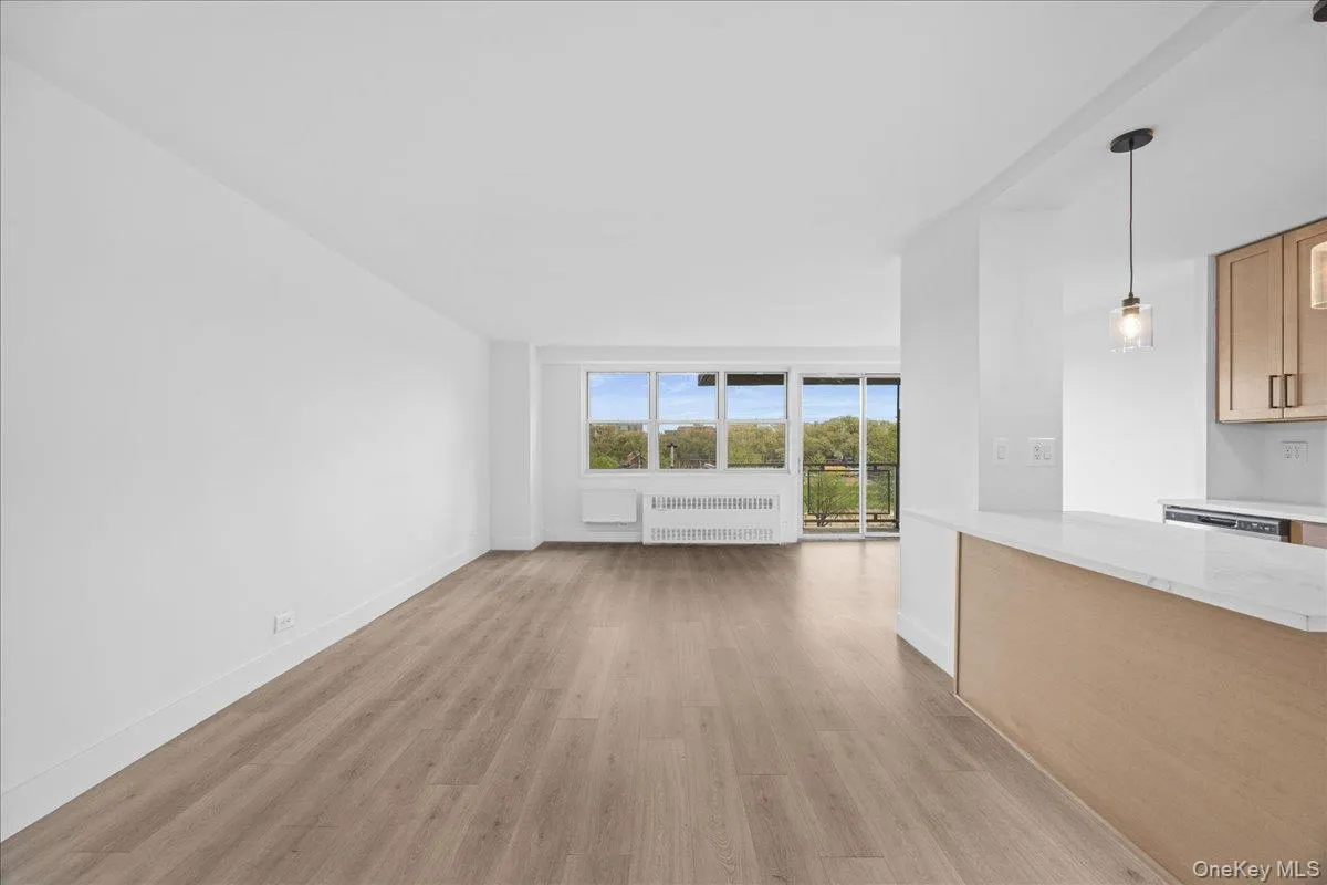 Open concept living space with light-tone vinyl flooring, white walls, and a large window with a balcony Open concept living space with light-tone vinyl flooring, white walls, and a large window with a balcony
