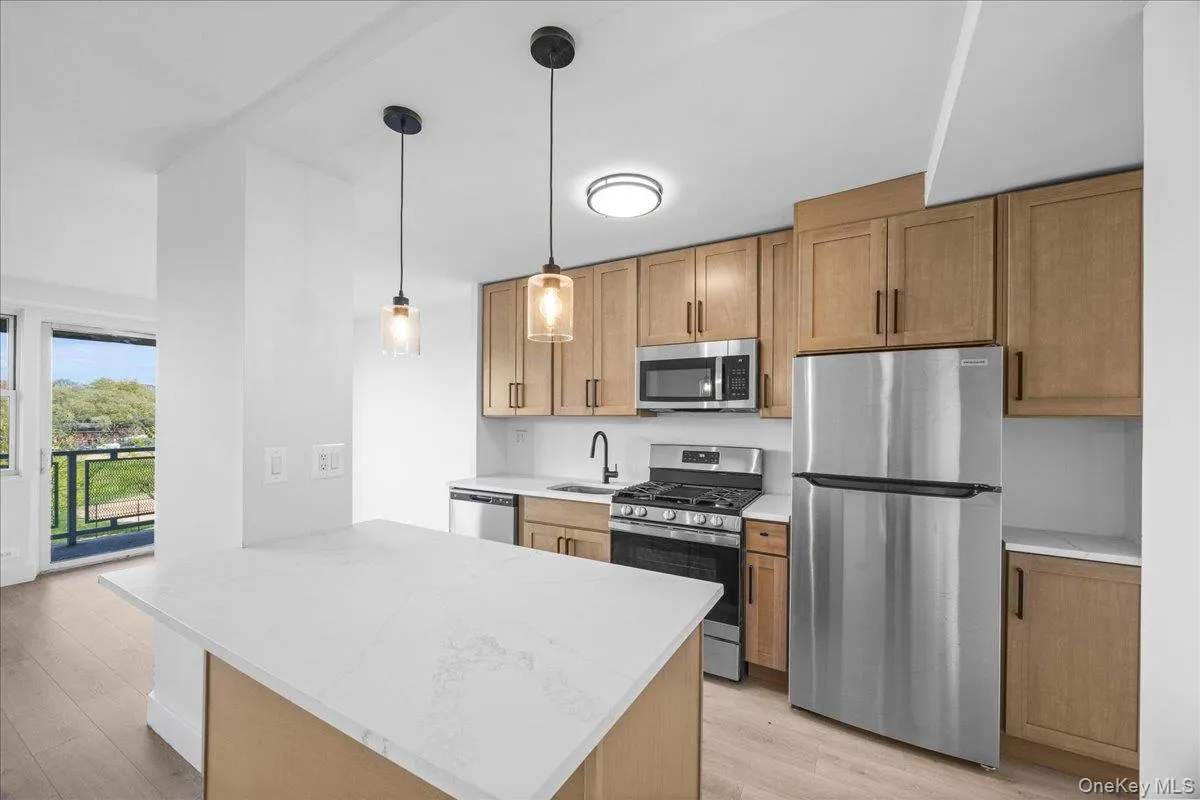 Modern kitchen featuring natural wood cabinetry, stainless steel appliances, and quartz countertops Modern kitchen featuring natural wood cabinetry, stainless steel appliances, and quartz countertops