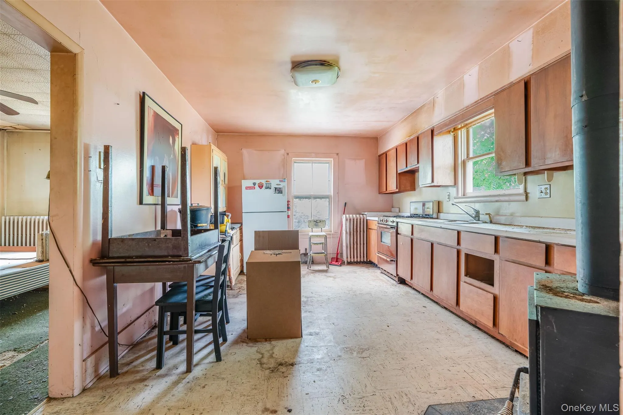 Kitchen with range with gas cooktop, freestanding refrigerator, light countertops, ceiling fan, and brown cabinetry Kitchen with range with gas cooktop, freestanding refrigerator, light countertops, ceiling fan, and brown cabinetry