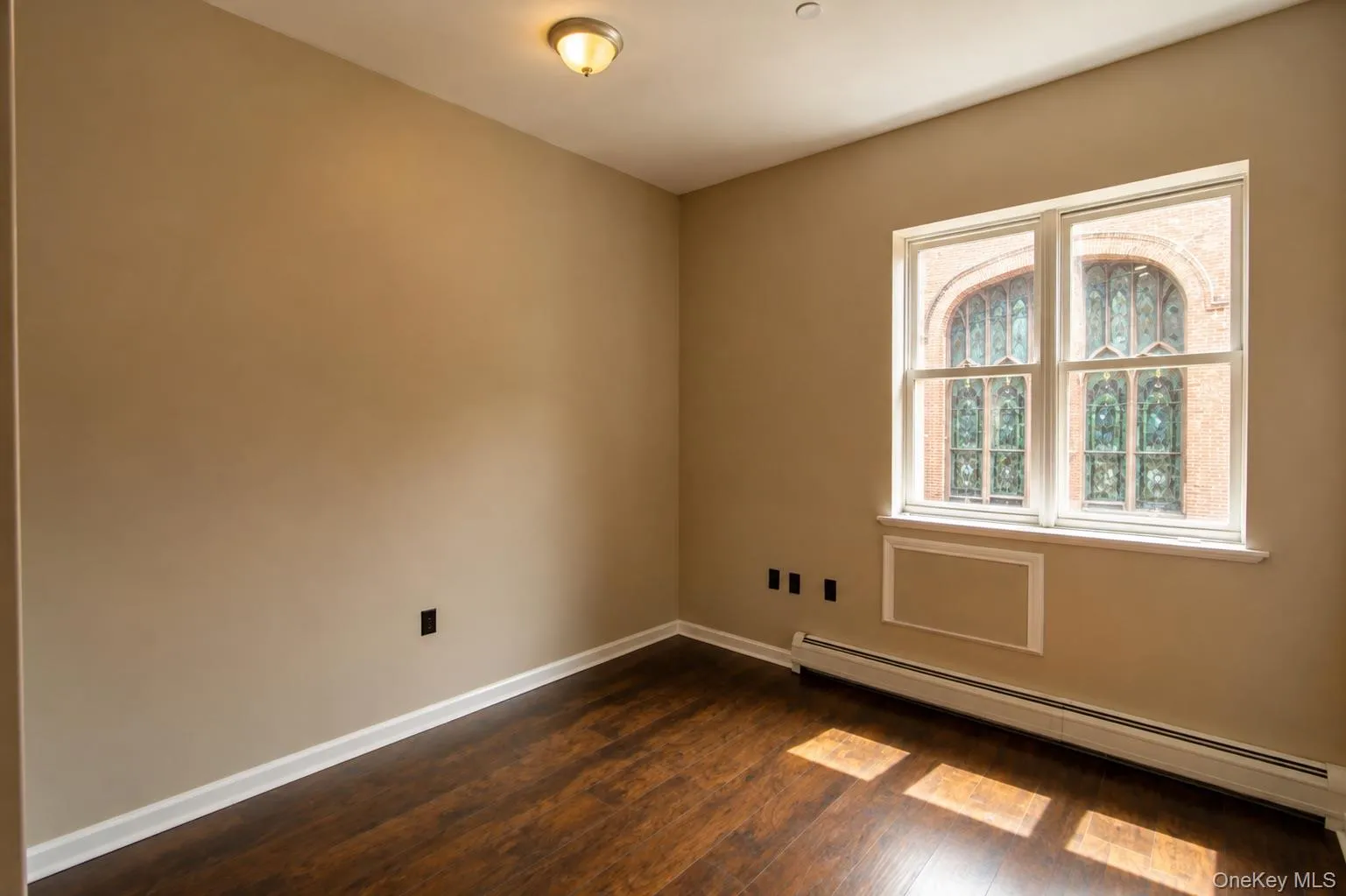 Warm neutral wall color, wood-finish flooring, white window trim, and baseboard heating Warm neutral wall color, wood-finish flooring, white window trim, and baseboard heating