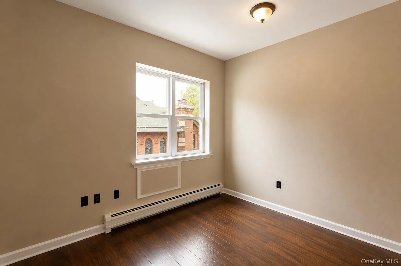 Bright corner bedroom featuring hardwood flooring, neutral wall finishes, and abundant natural light from a large double-hung window Bright corner bedroom featuring hardwood flooring, neutral wall finishes, and abundant natural light from a large double-hung window