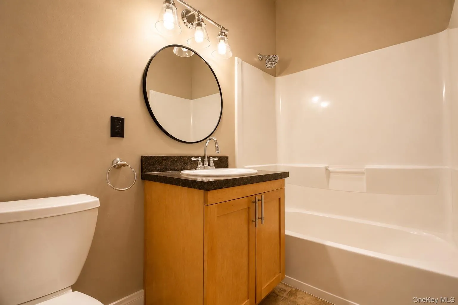 Vanity with a dark countertop and undermount sink, illuminated by a three-light fixture Vanity with a dark countertop and undermount sink, illuminated by a three-light fixture