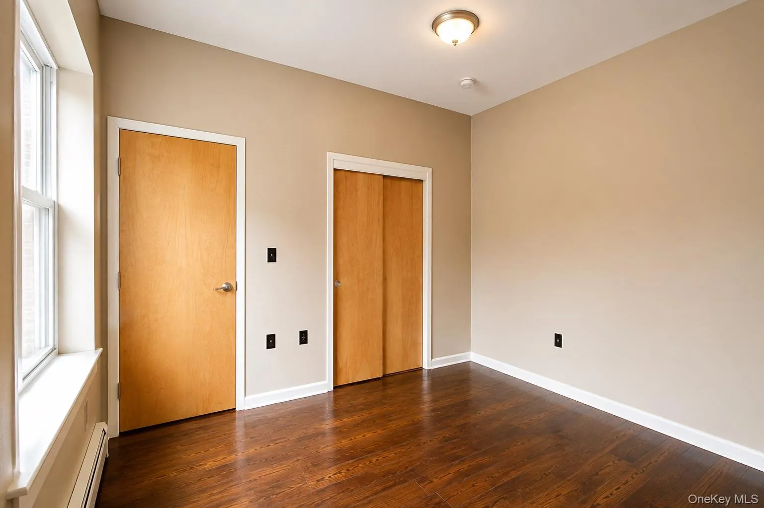 Dark wood-finish flooring, two natural wood doors with brushed nickel hardware, white trim, and a ceiling-mounted light fixture Dark wood-finish flooring, two natural wood doors with brushed nickel hardware, white trim, and a ceiling-mounted light fixture