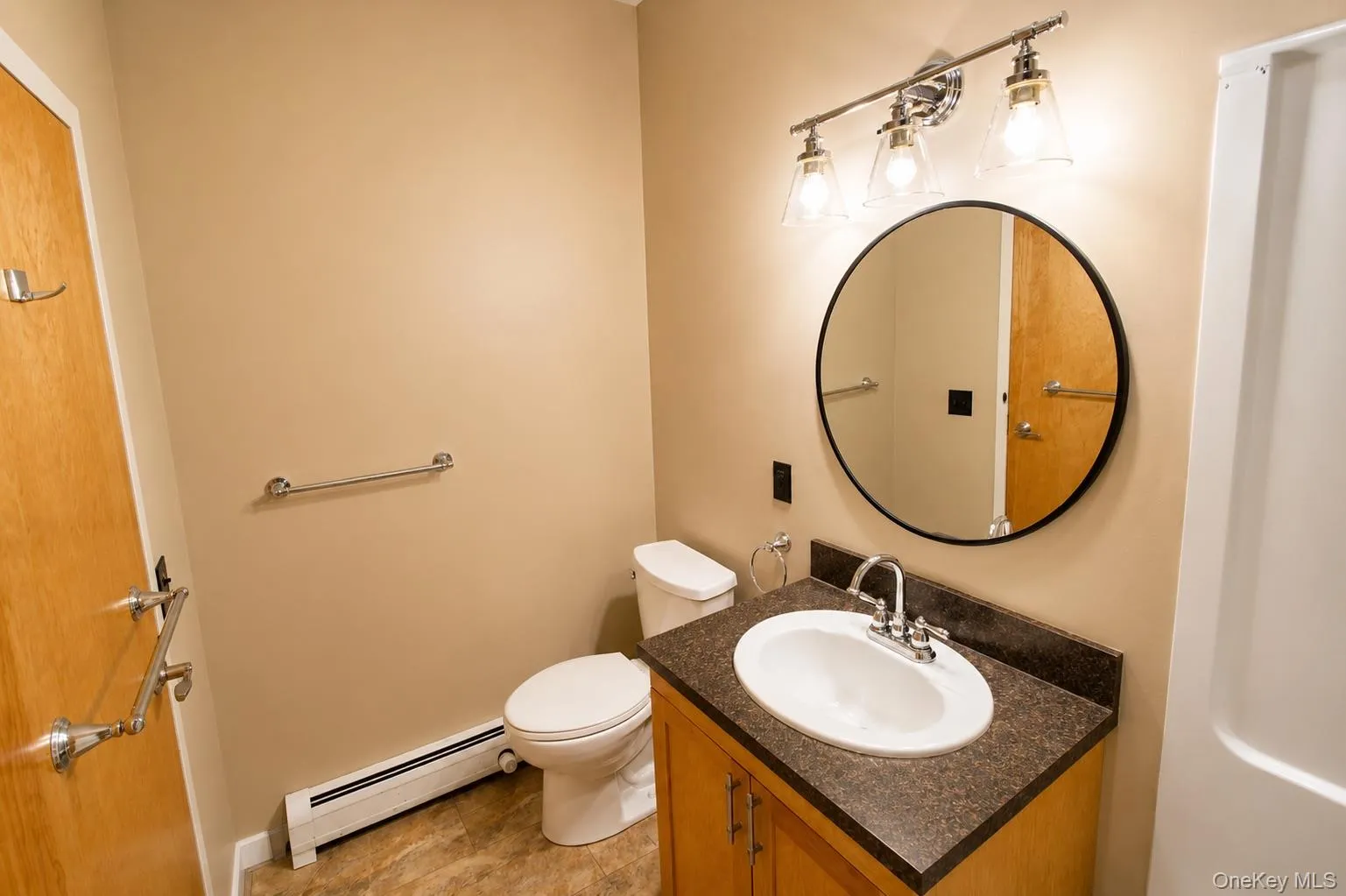 Vanity with a white oval sink, dark countertop, and wood-finish cabinetry Vanity with a white oval sink, dark countertop, and wood-finish cabinetry