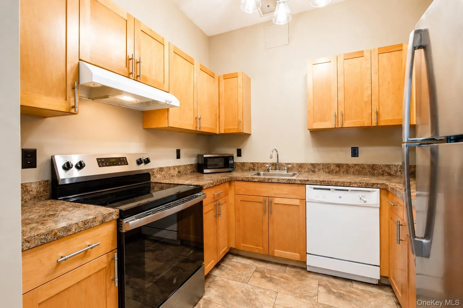Kitchen featuring light wood-finish cabinetry, patterned countertops, stainless steel range, stainless steel refrigerator, and a built-in dishwasher Kitchen featuring light wood-finish cabinetry, patterned countertops, stainless steel range, stainless steel refrigerator, and a built-in dishwasher
