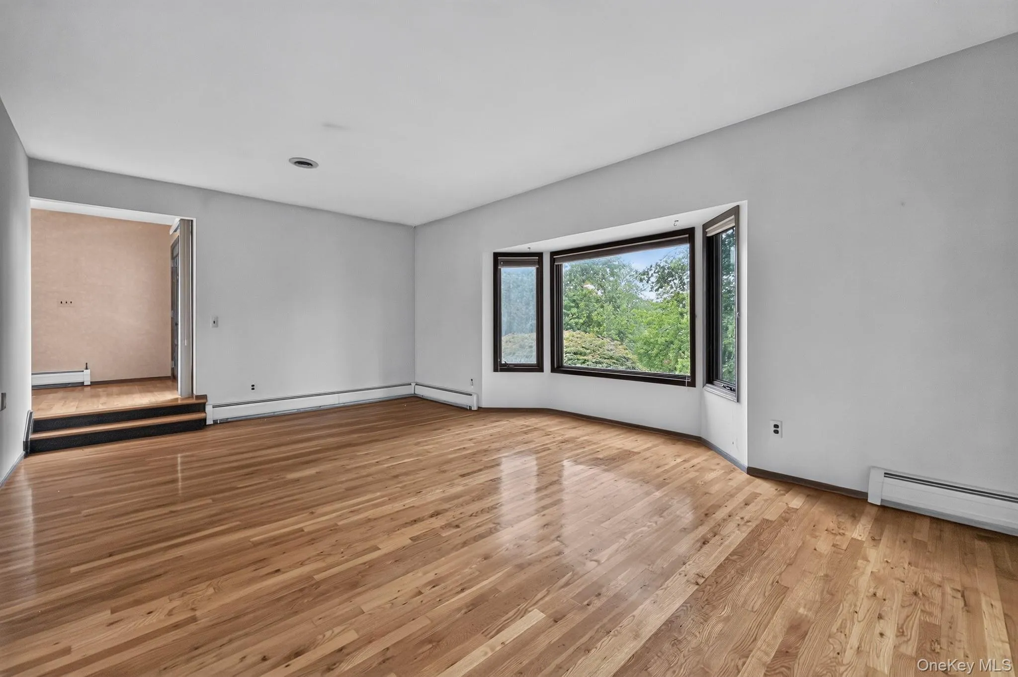 An expansive, formal step-down living room with soaring high ceilings, freshly polished solid hardwood floors, and a large architectural bow window letting in natural light. An expansive, formal step-down living room with soaring high ceilings, freshly polished solid hardwood floors, and a large architectural bow window letting in natural light.