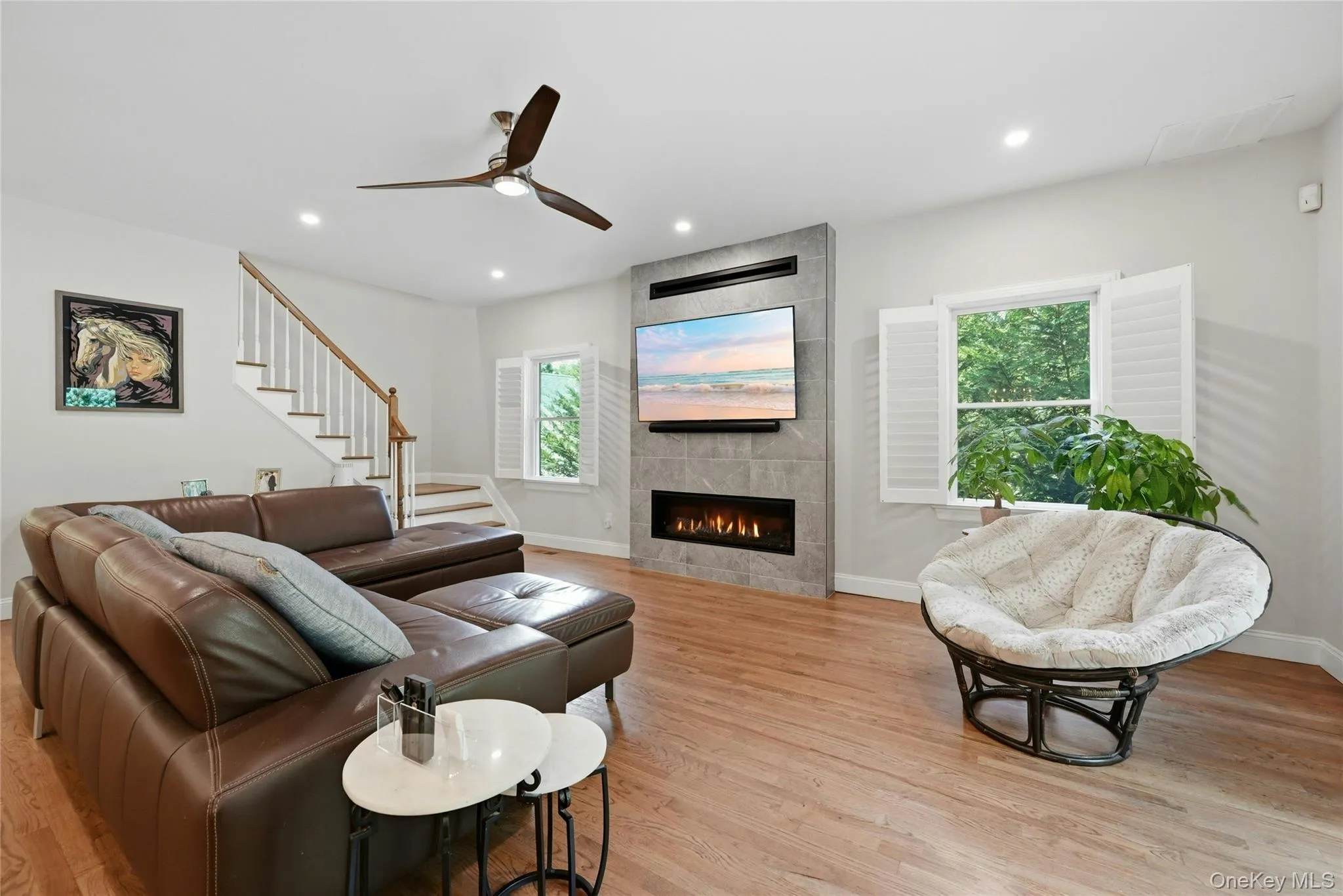 Open-concept living space featuring hardwood flooring, a contemporary ceiling fan, and a linear gas fireplace with stone surround and mounted television Open-concept living space featuring hardwood flooring, a contemporary ceiling fan, and a linear gas fireplace with stone surround and mounted television