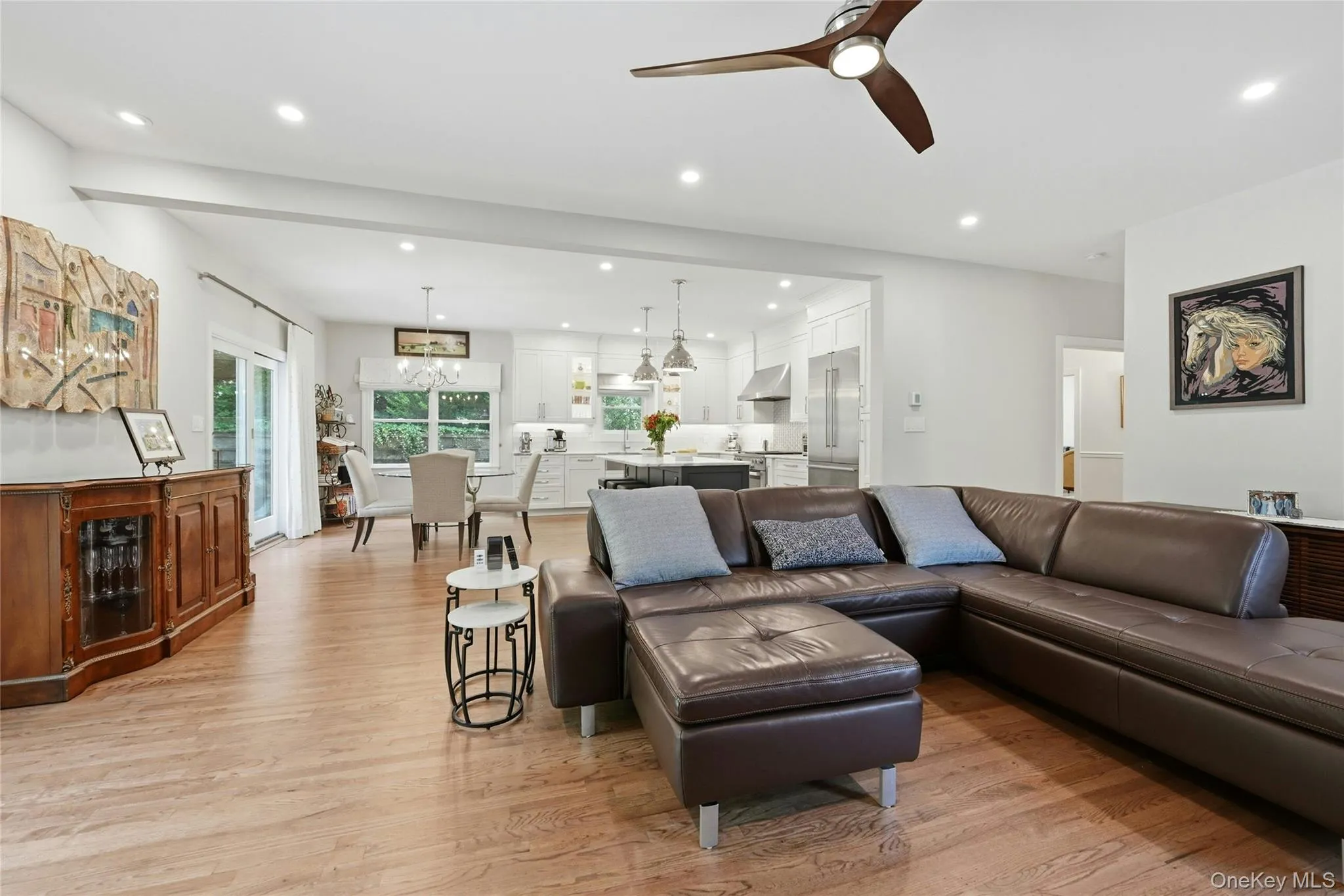 Open-concept living area featuring a brown leather sectional, wood-finish flooring throughout, and abundant recessed lighting Open-concept living area featuring a brown leather sectional, wood-finish flooring throughout, and abundant recessed lighting