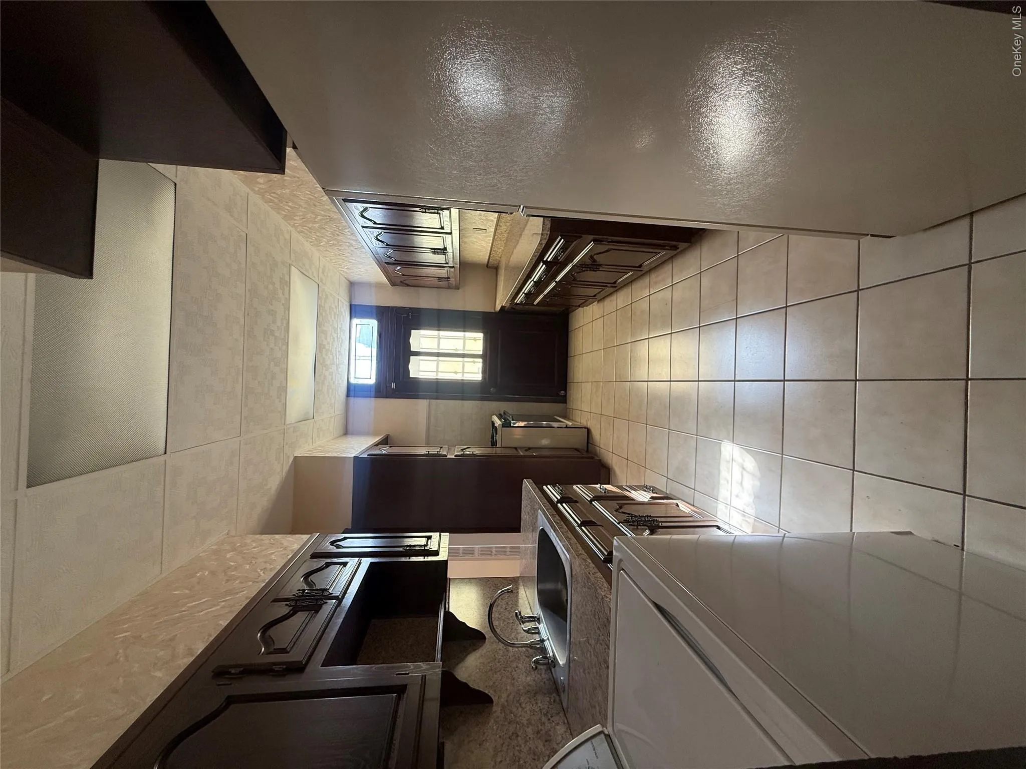 Kitchen with fridge, washer / dryer, light tile patterned floors, a paneled ceiling, and dark brown cabinets Kitchen with fridge, washer / dryer, light tile patterned floors, a paneled ceiling, and dark brown cabinets