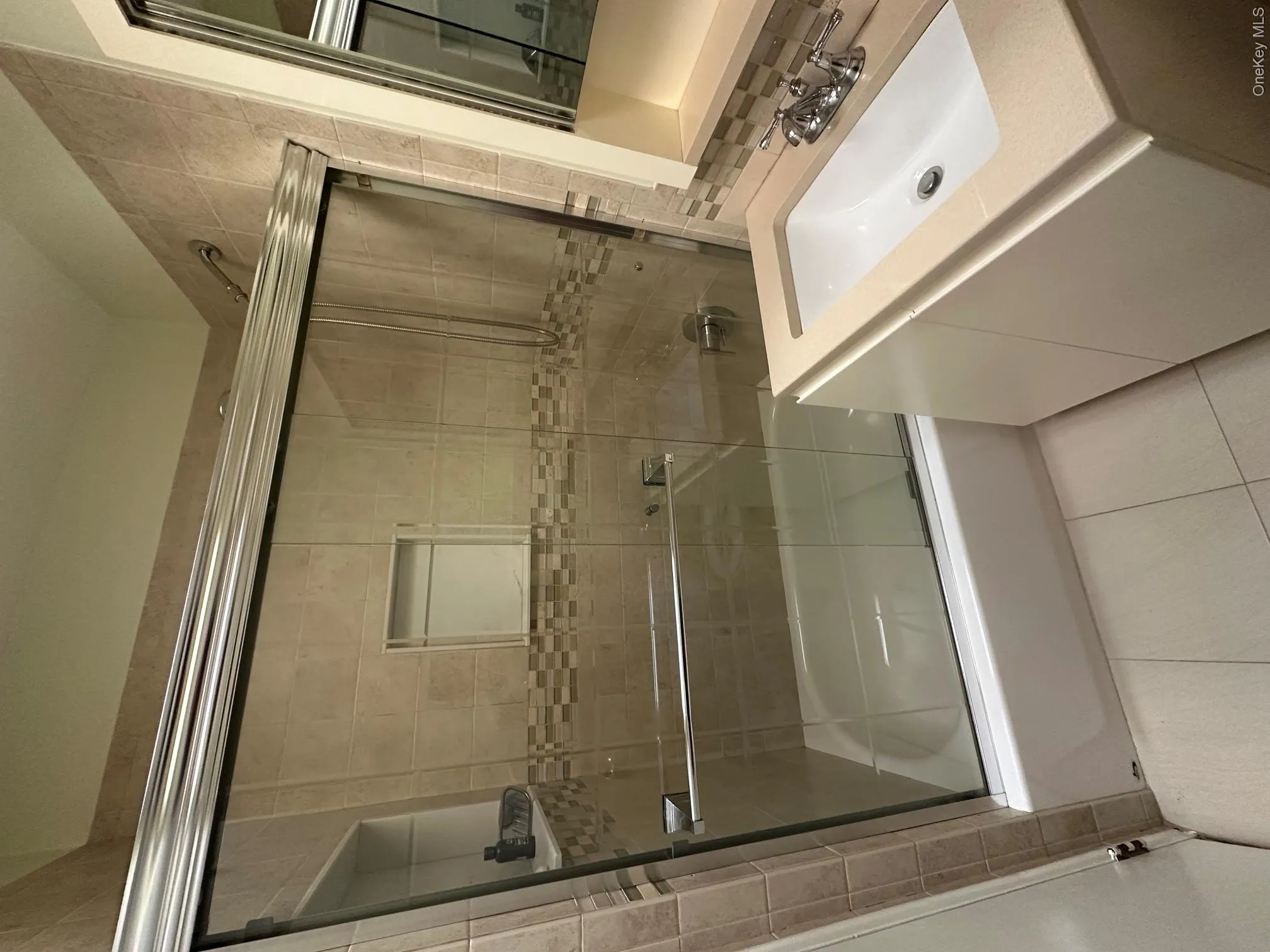 Ceramic tile flooring, tiled shower with glass sliding doors, built-in shower niche, integrated vanity sink, and mirrored medicine cabinet Ceramic tile flooring, tiled shower with glass sliding doors, built-in shower niche, integrated vanity sink, and mirrored medicine cabinet