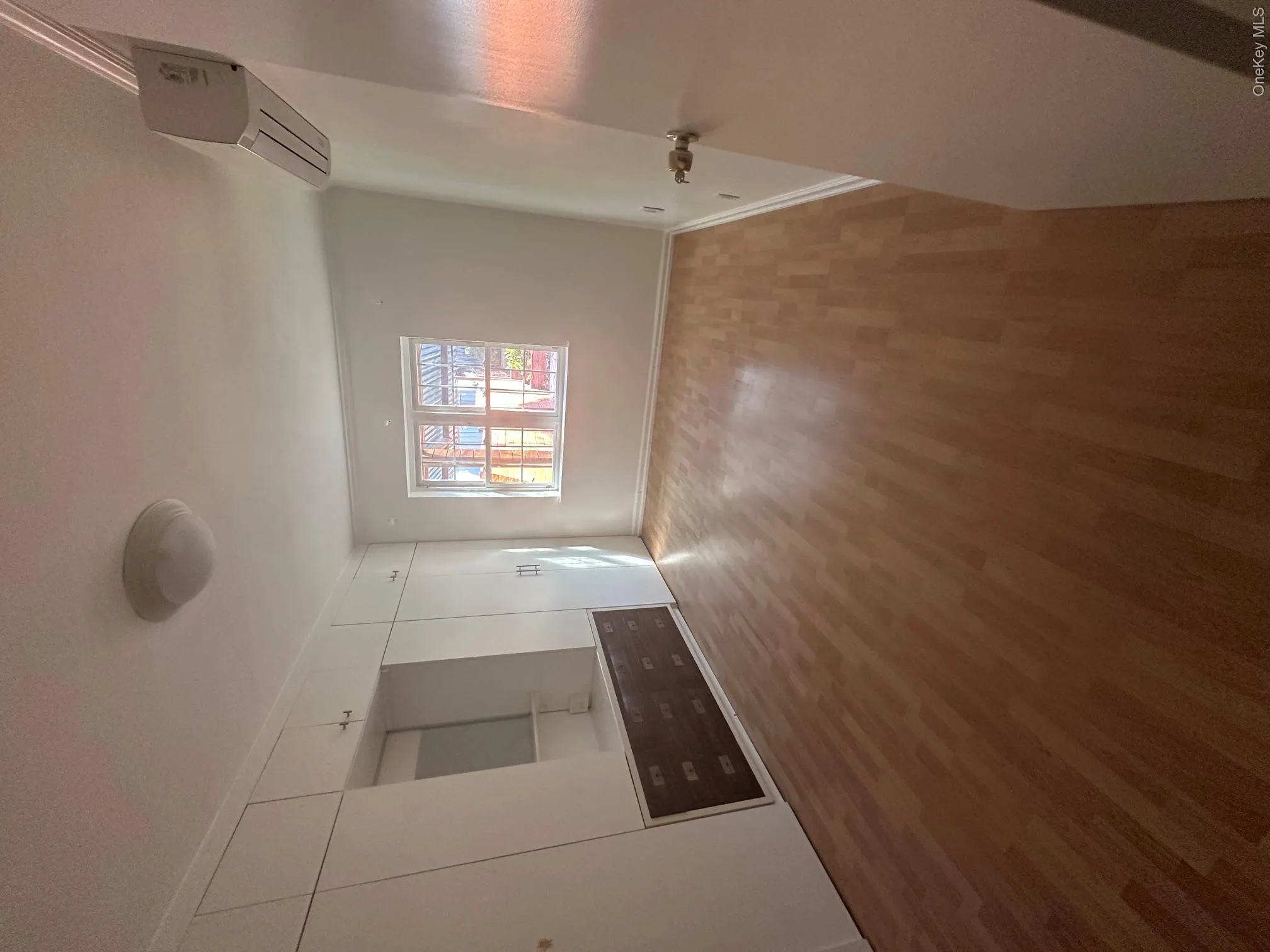 Wood-finish flooring, built-in cabinetry with mirror, window with white trim, wall-mounted air conditioning unit, and ceiling-mounted light fixture Wood-finish flooring, built-in cabinetry with mirror, window with white trim, wall-mounted air conditioning unit, and ceiling-mounted light fixture