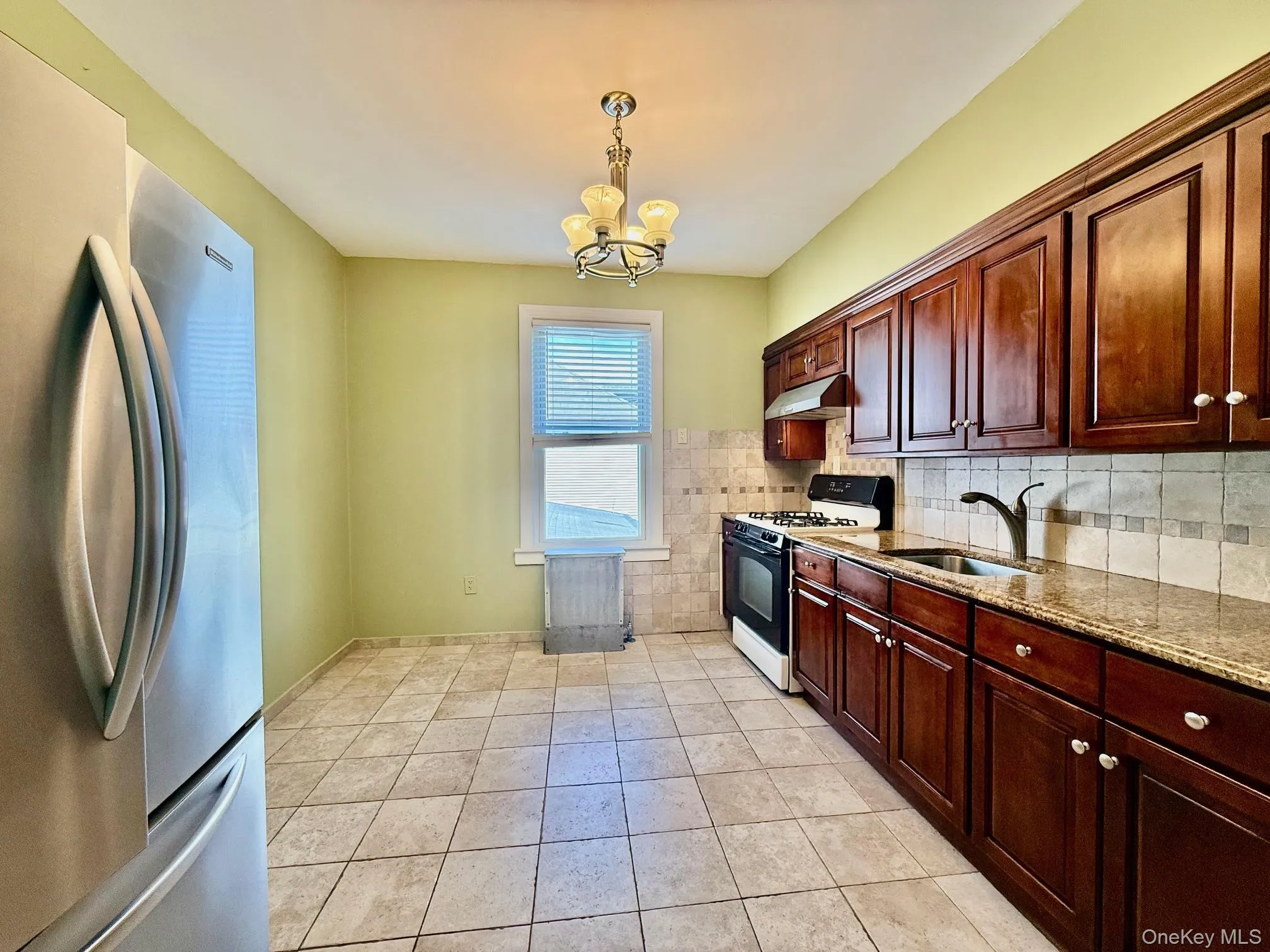 Kitchen featuring wood-finish cabinetry, tile flooring, and a stainless steel refrigerator Kitchen featuring wood-finish cabinetry, tile flooring, and a stainless steel refrigerator