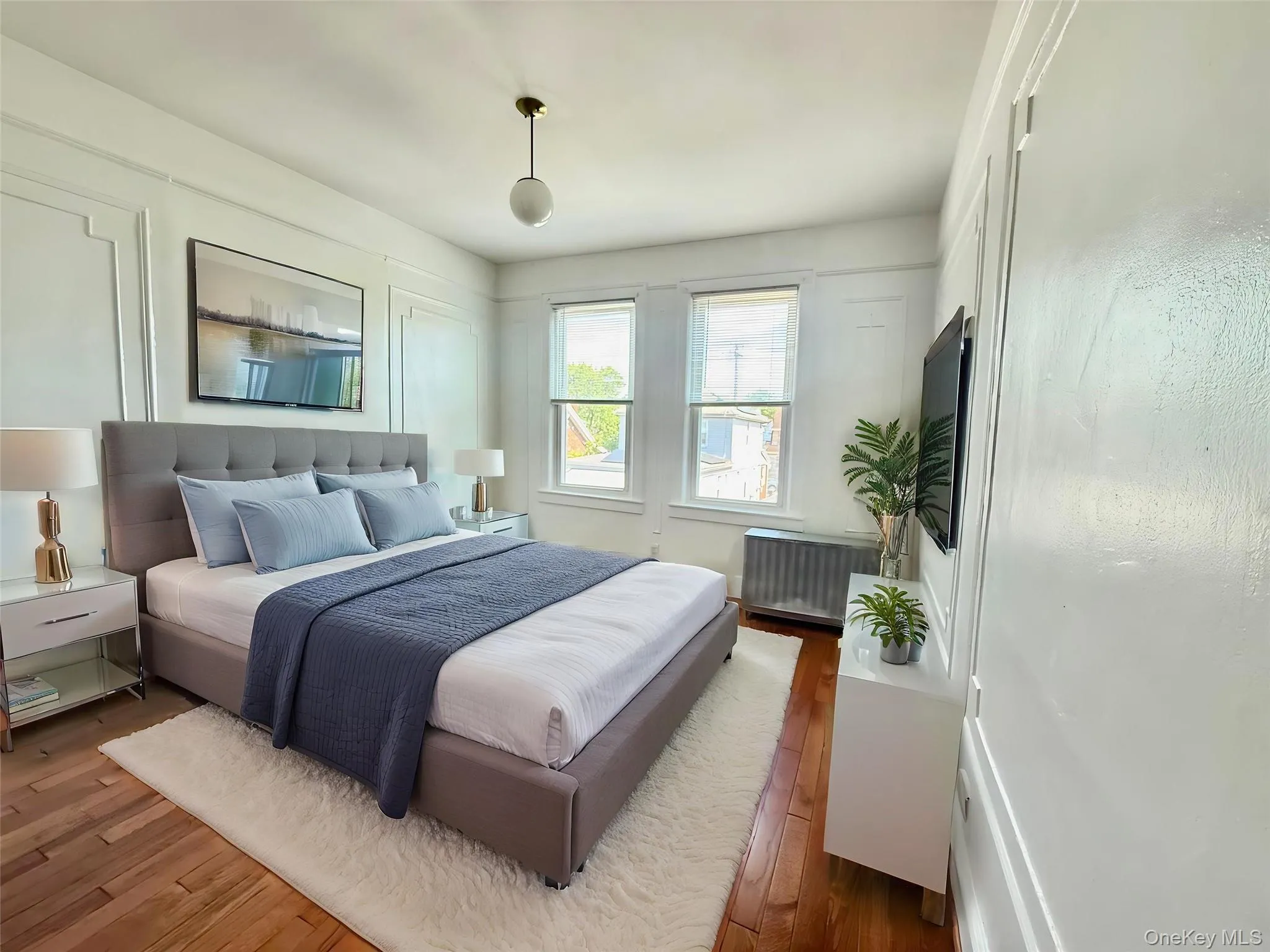Hardwood flooring, decorative wall molding, window with natural light, wall-mounted television, and a ceiling light fixture Hardwood flooring, decorative wall molding, window with natural light, wall-mounted television, and a ceiling light fixture