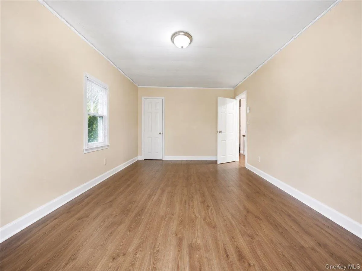 Wood-finish flooring, neutral wall tones, white trim, and a ceiling-mounted light fixture Wood-finish flooring, neutral wall tones, white trim, and a ceiling-mounted light fixture