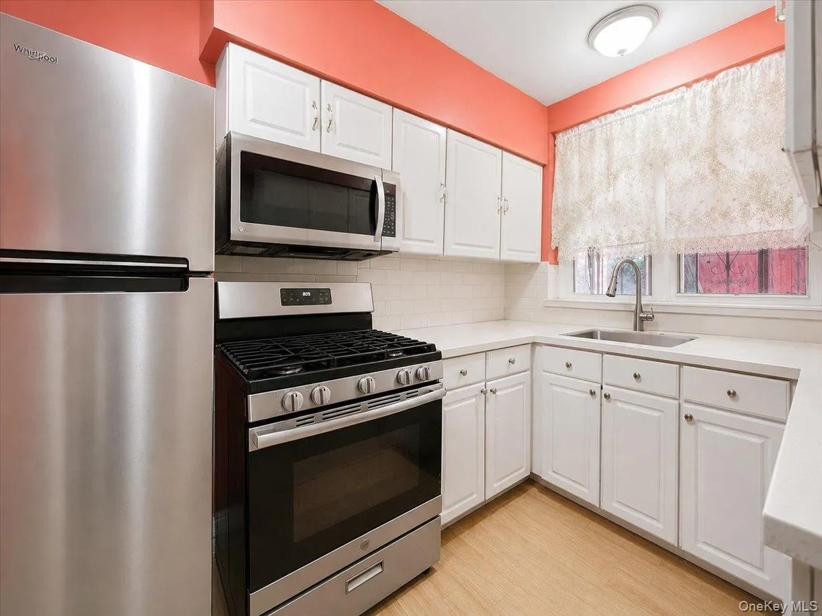White cabinetry with stainless steel hardware, stainless steel appliances, white subway tile backsplash, light-toned countertops, and wood-finish flooring White cabinetry with stainless steel hardware, stainless steel appliances, white subway tile backsplash, light-toned countertops, and wood-finish flooring