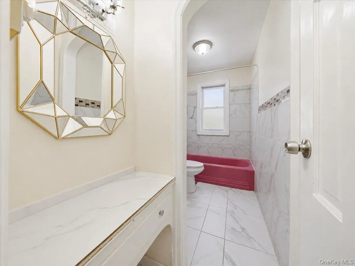 Bathroom featuring white tile flooring, tiled walls with an accent border, a window, and a built-in bathtub Bathroom featuring white tile flooring, tiled walls with an accent border, a window, and a built-in bathtub