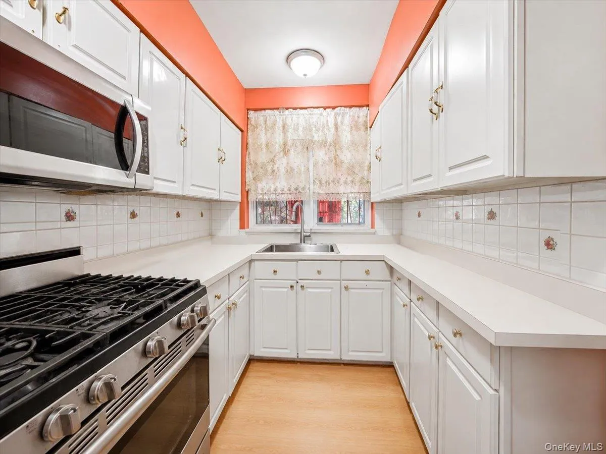 Galley kitchen featuring white cabinetry, light countertops, tile backsplash, stainless steel range, and an integrated microwave Galley kitchen featuring white cabinetry, light countertops, tile backsplash, stainless steel range, and an integrated microwave