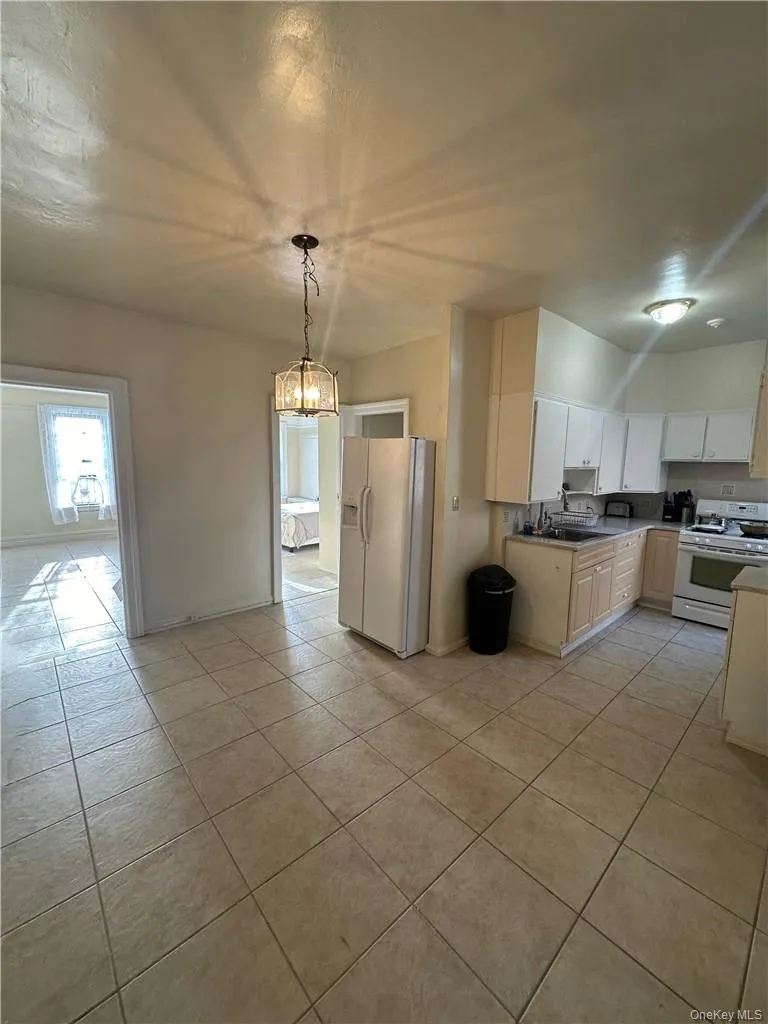Kitchen featuring decorative light fixtures, white appliances, and light tile floors Kitchen featuring decorative light fixtures, white appliances, and light tile floors