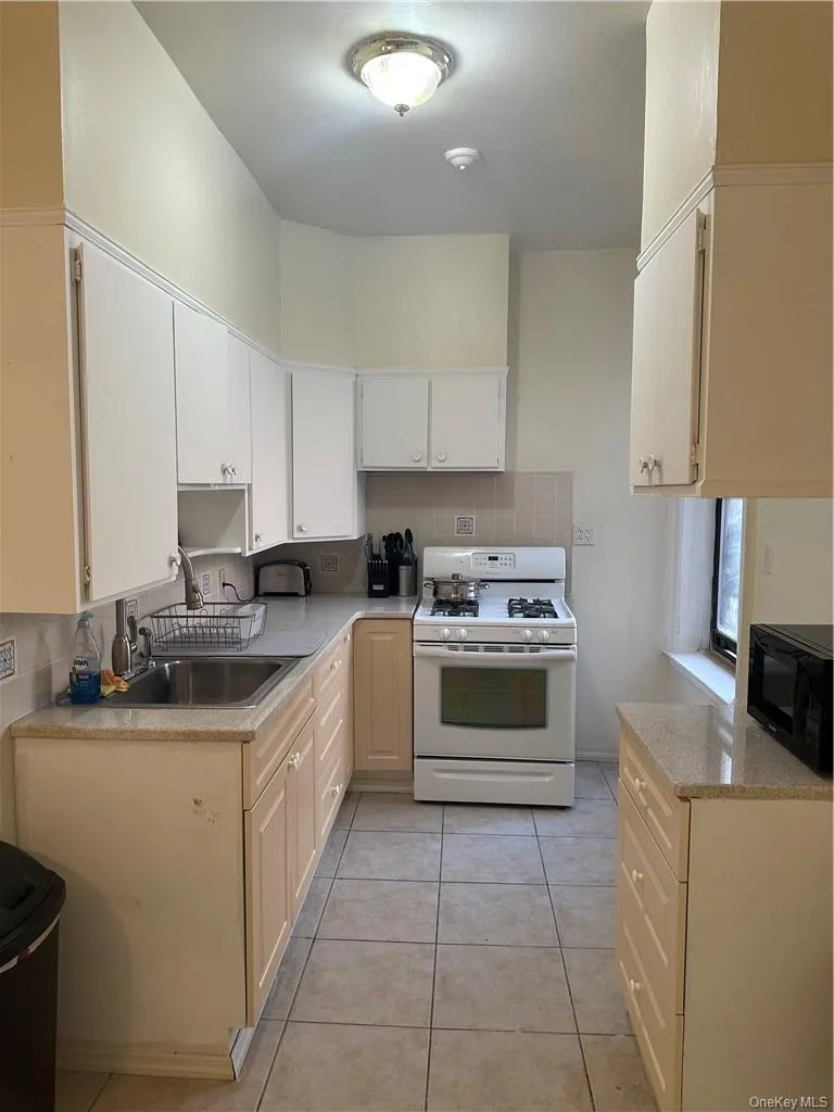 Kitchen featuring backsplash, light tile floors, sink, and white electric range Kitchen featuring backsplash, light tile floors, sink, and white electric range
