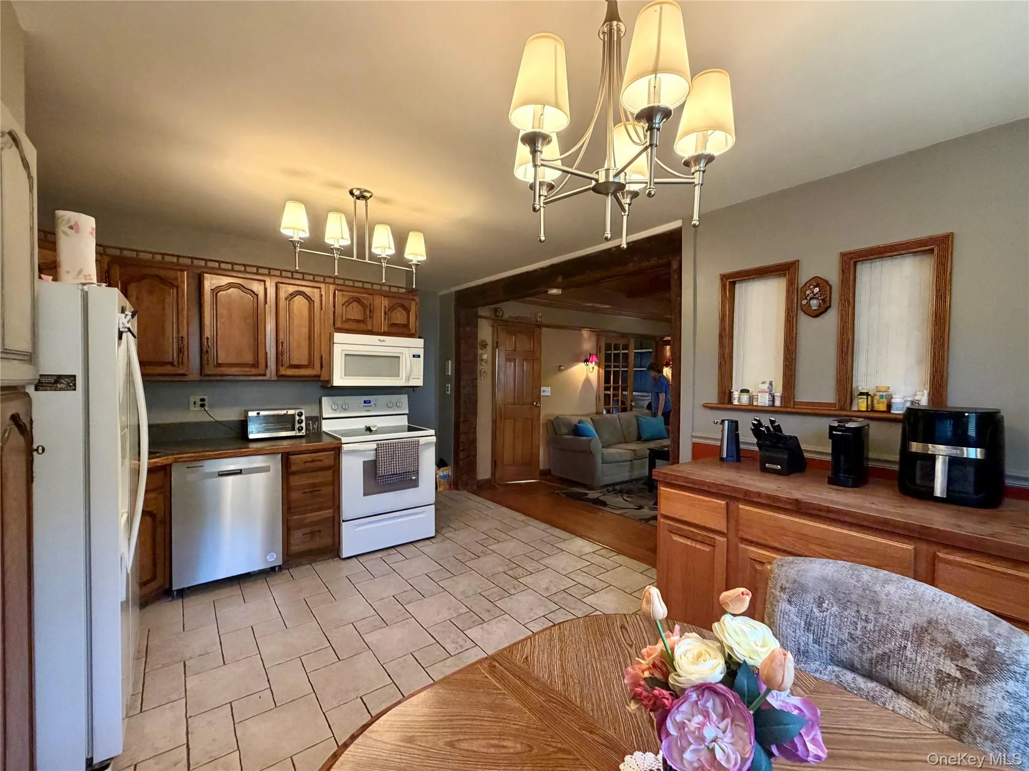 Kitchen featuring tile flooring, wood-finish cabinetry, stainless steel dishwasher, white range, and a ceiling-mounted chandelier Kitchen featuring tile flooring, wood-finish cabinetry, stainless steel dishwasher, white range, and a ceiling-mounted chandelier
