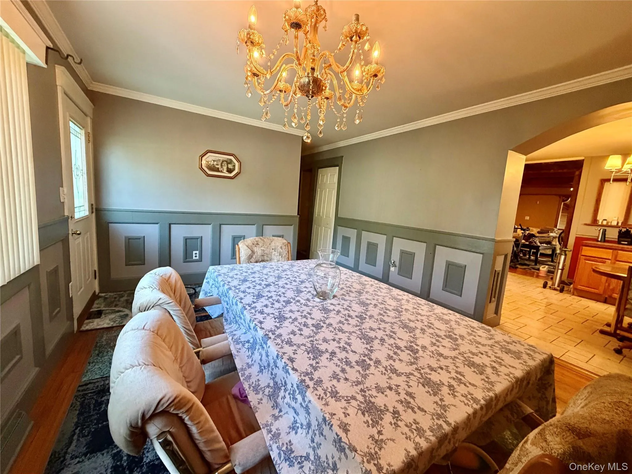 Hardwood-flooring, wainscoting details, ornate chandelier, crown molding, and an arched entryway Hardwood-flooring, wainscoting details, ornate chandelier, crown molding, and an arched entryway