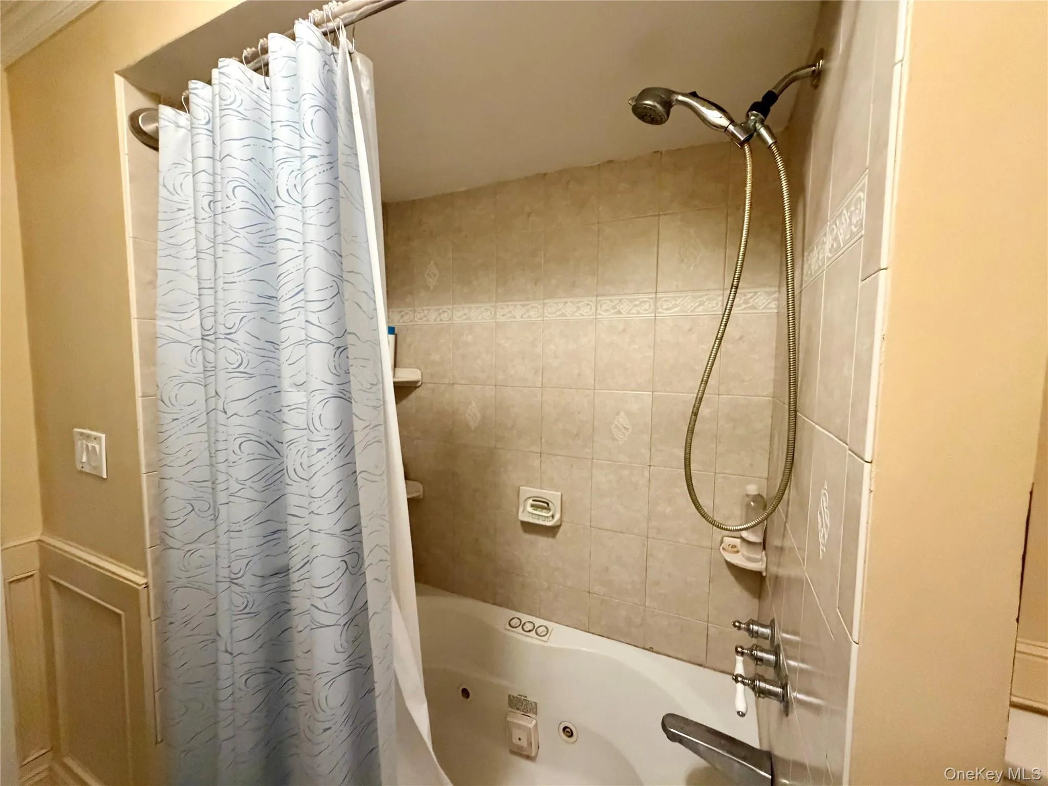 Built-in jetted tub with tiled surround, handheld shower fixture, and wall-mounted shower head Built-in jetted tub with tiled surround, handheld shower fixture, and wall-mounted shower head
