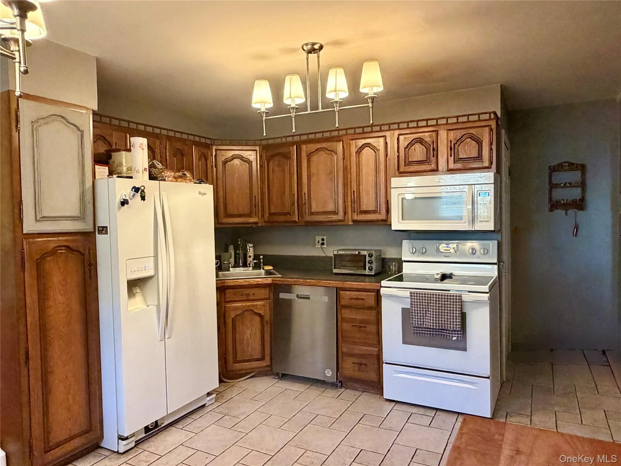 Kitchen featuring wood cabinetry, a white refrigerator, a white electric range, an over-range microwave, and a stainless steel dishwasher Kitchen featuring wood cabinetry, a white refrigerator, a white electric range, an over-range microwave, and a stainless steel dishwasher