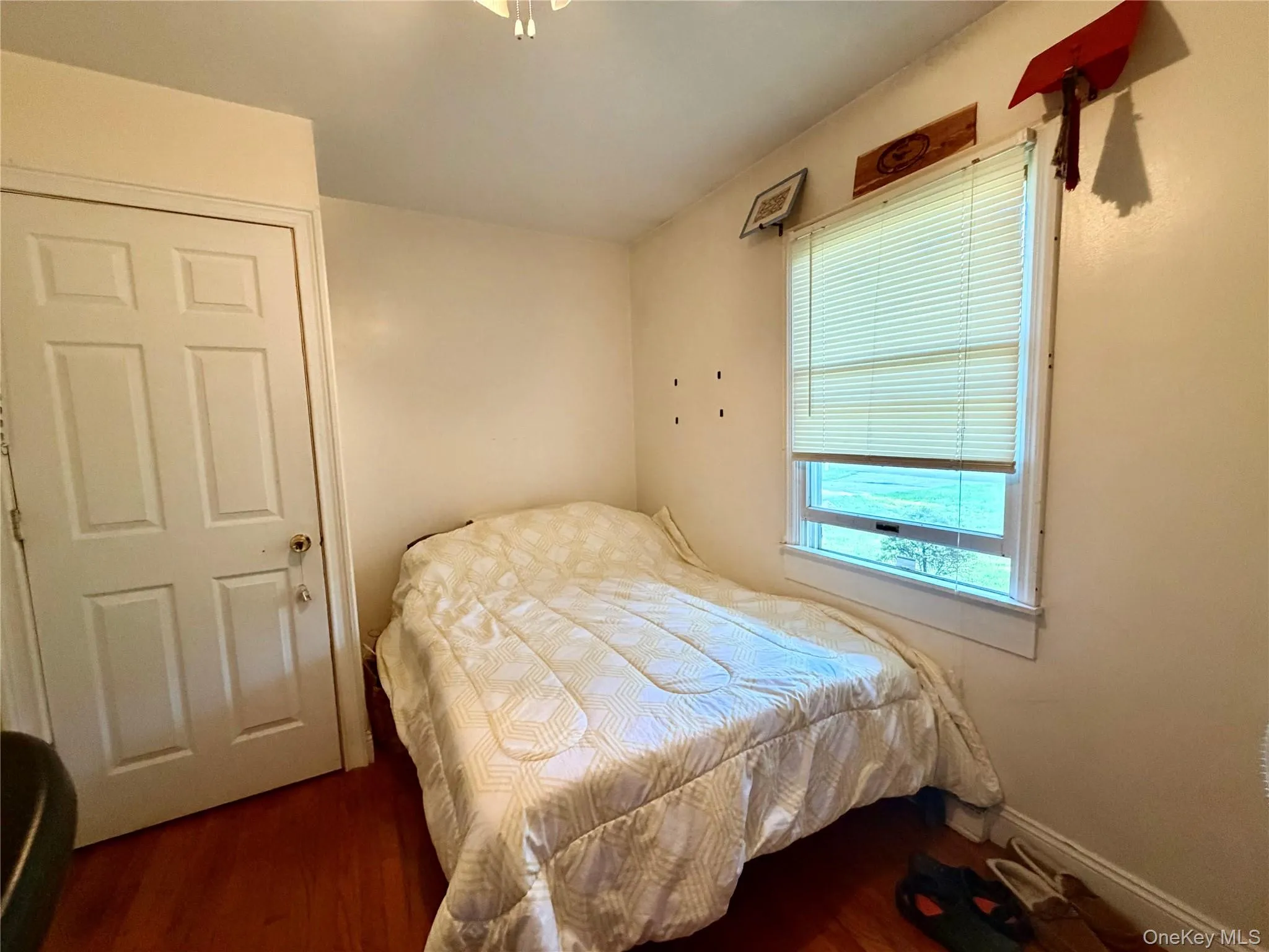 Wood-finish flooring with light-toned walls, a white paneled door, and a single window with blinds Wood-finish flooring with light-toned walls, a white paneled door, and a single window with blinds